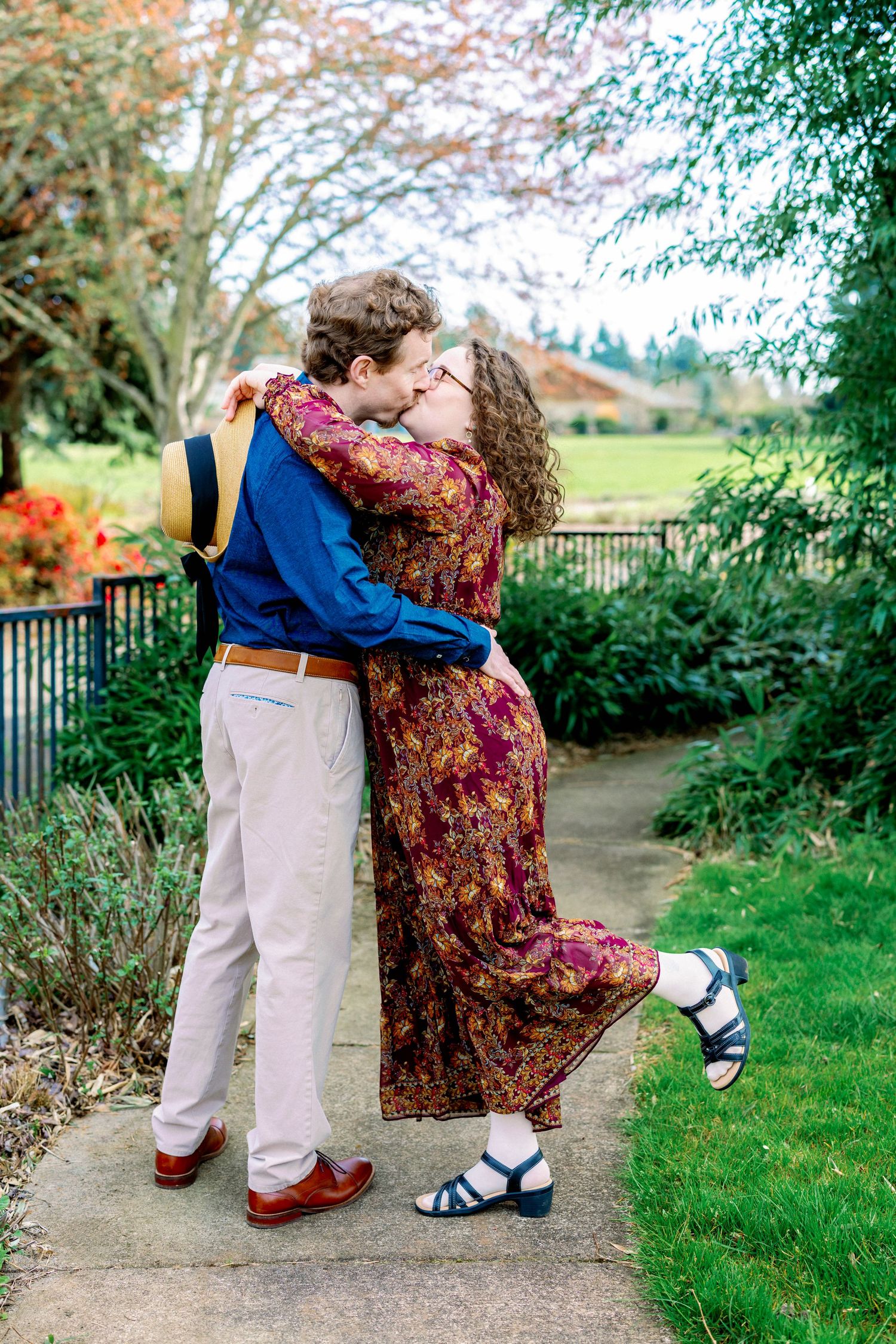 A couple performs a romantic dance dip pose on a garden pathway surrounded by greenery.