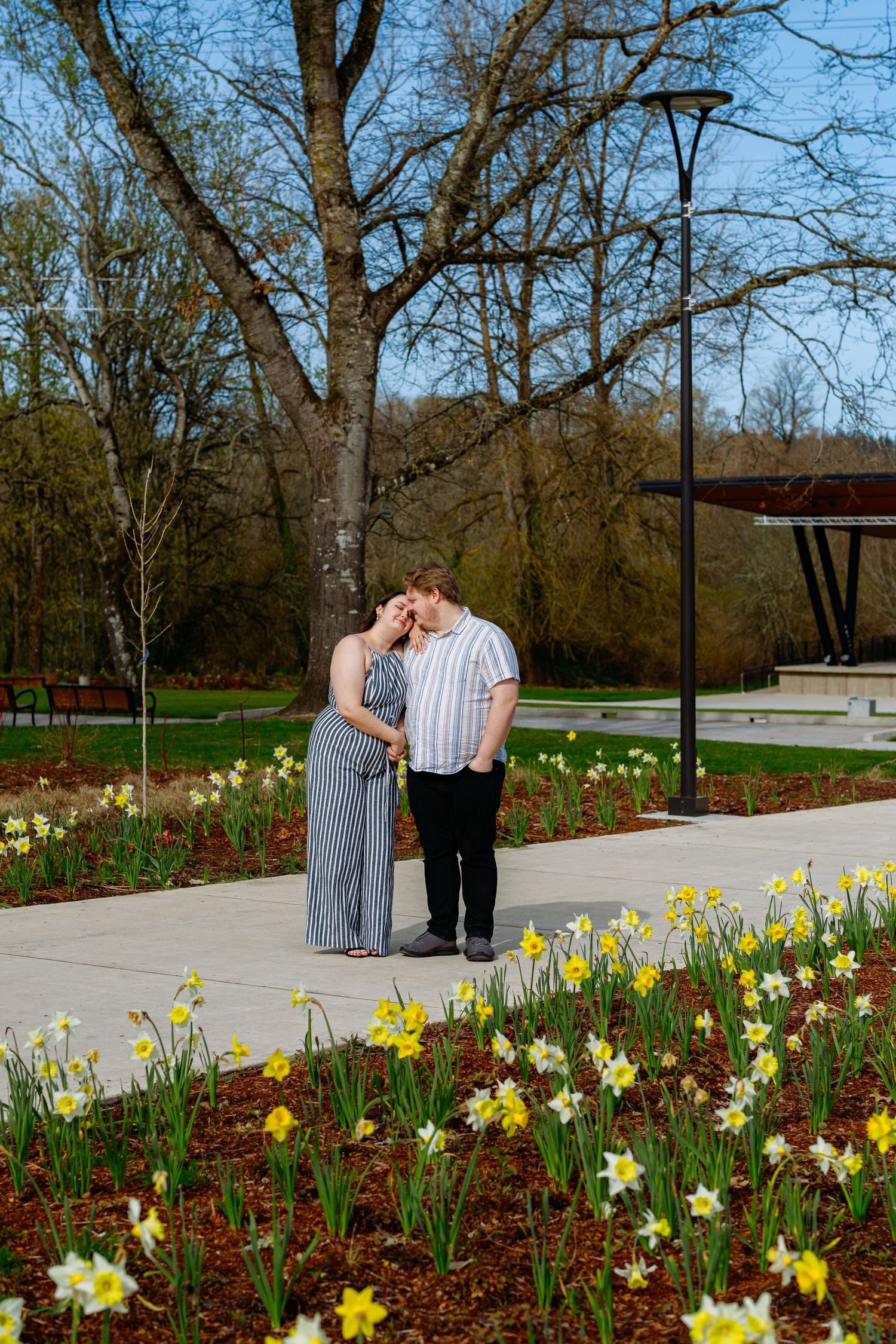 A couple shares tender moments along a garden path with blooming daffodils and spring flowers.
