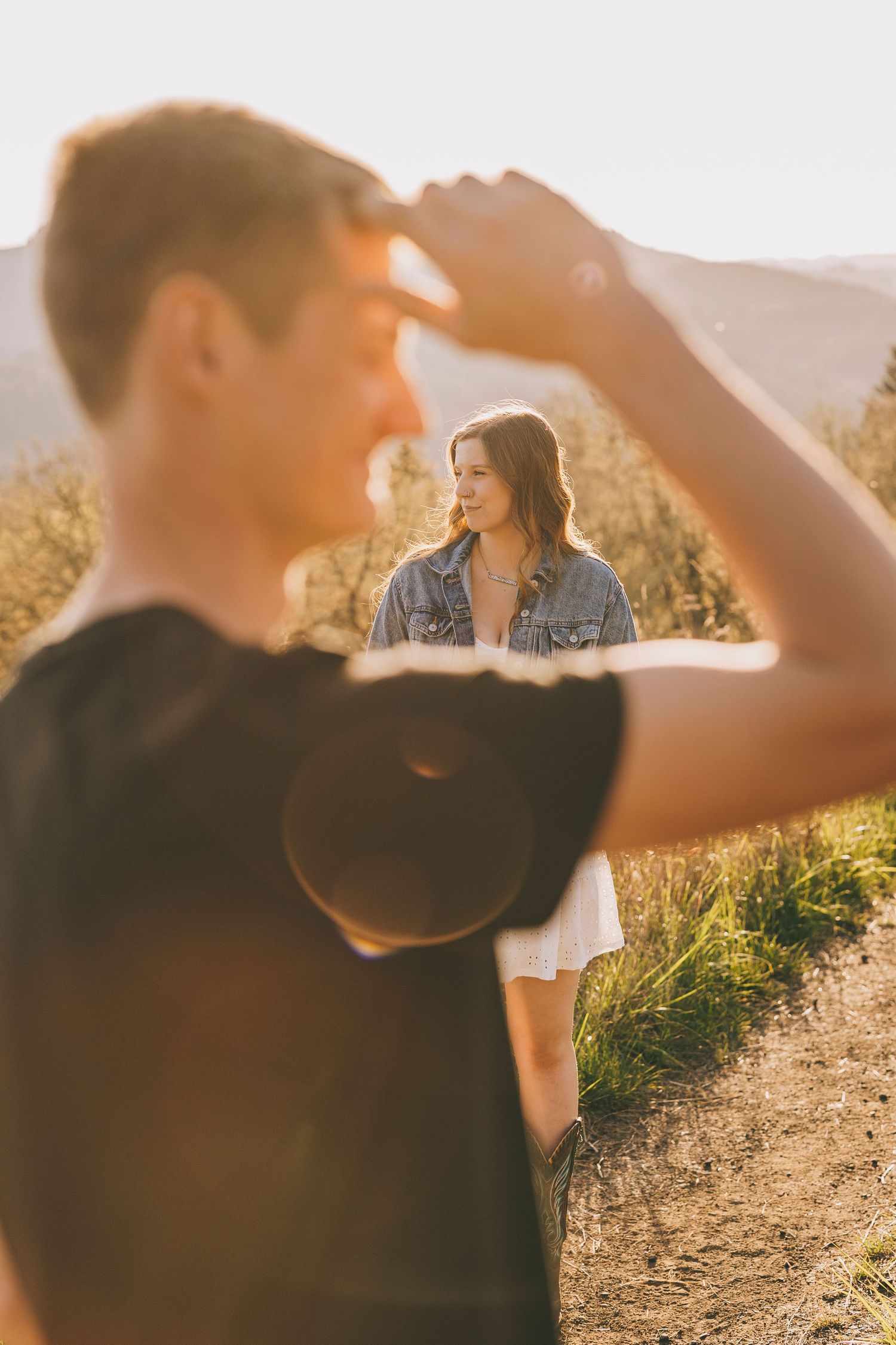 A romantic photoshoot in a sun-drenched field shows two people in casual attire enjoying a warm afternoon.