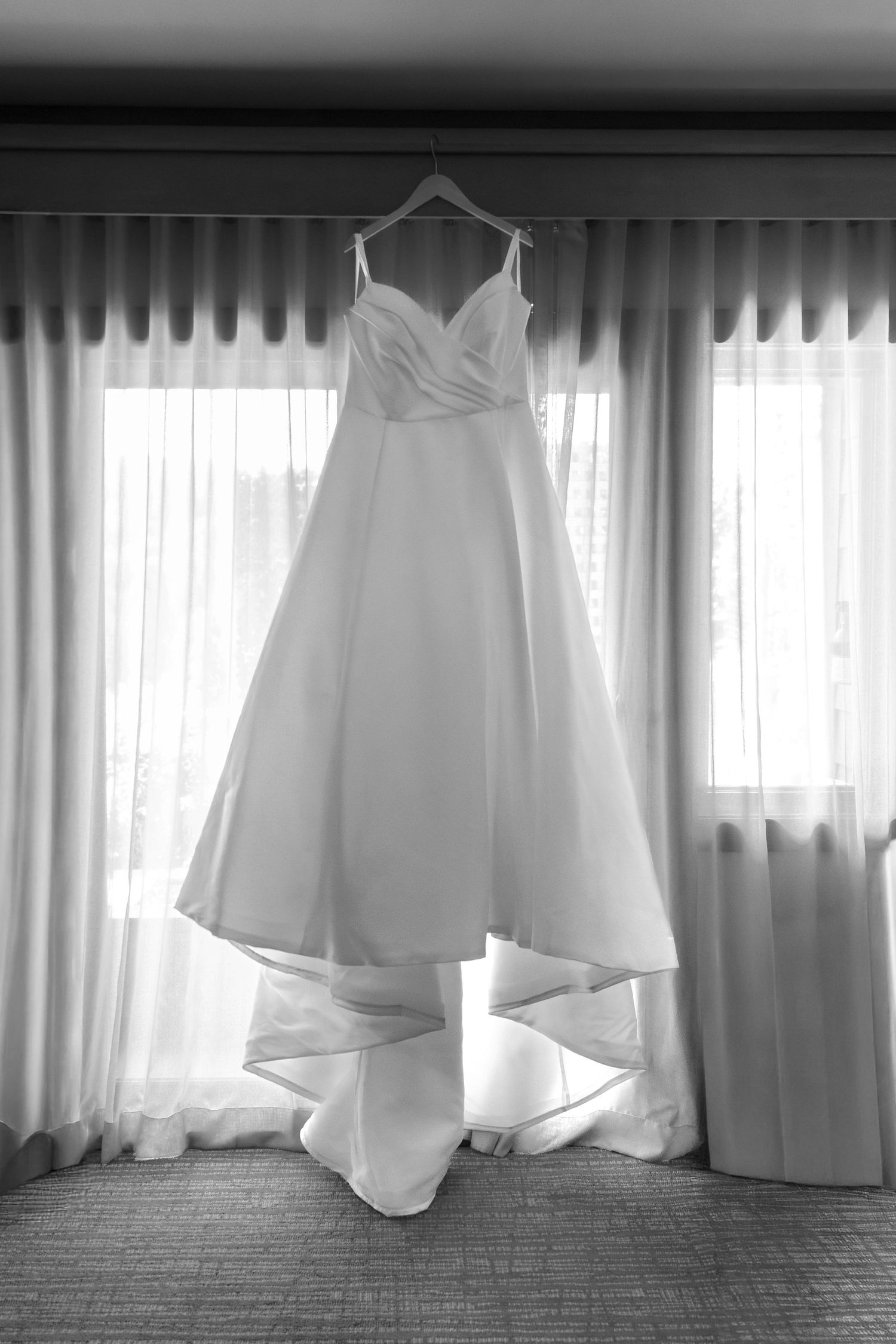 Five elegant white wedding dresses hanging in a row against sheer curtains in natural light.