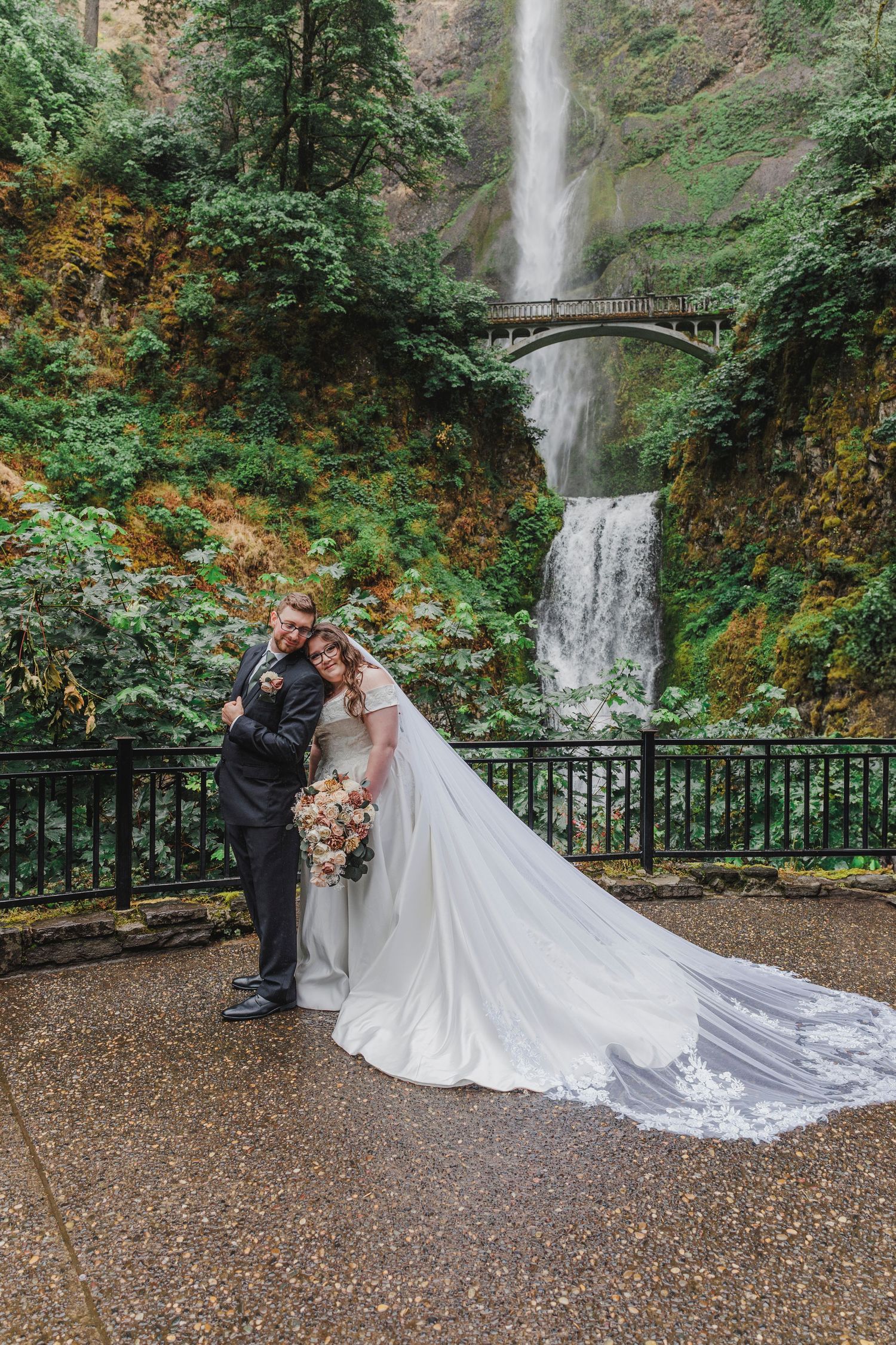 A wedding couple poses in front of Multnomah Falls with a flowing white dress train on display.