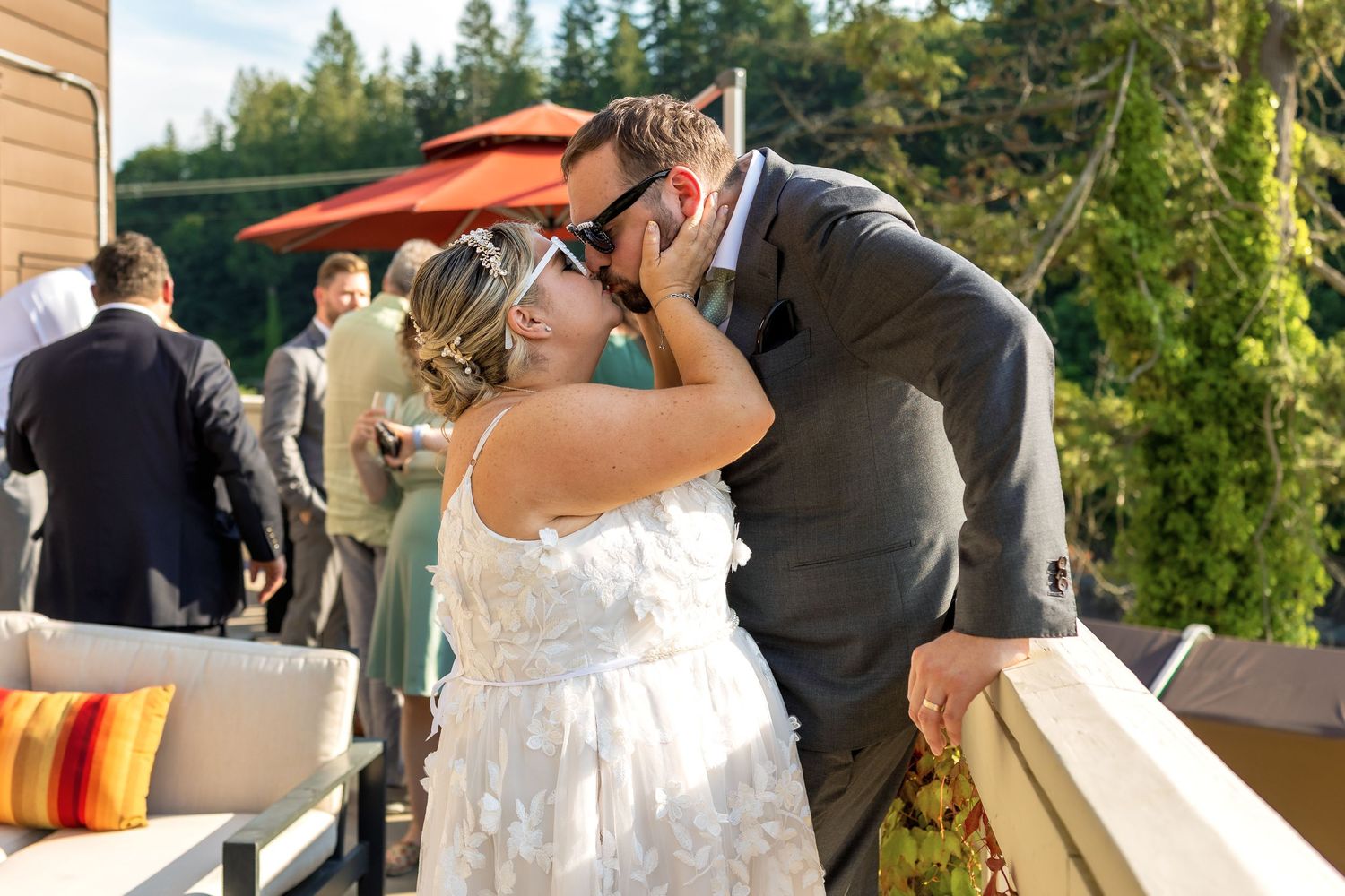 Outdoor wedding celebration with guests gathered on a patio surrounded by evergreen trees.