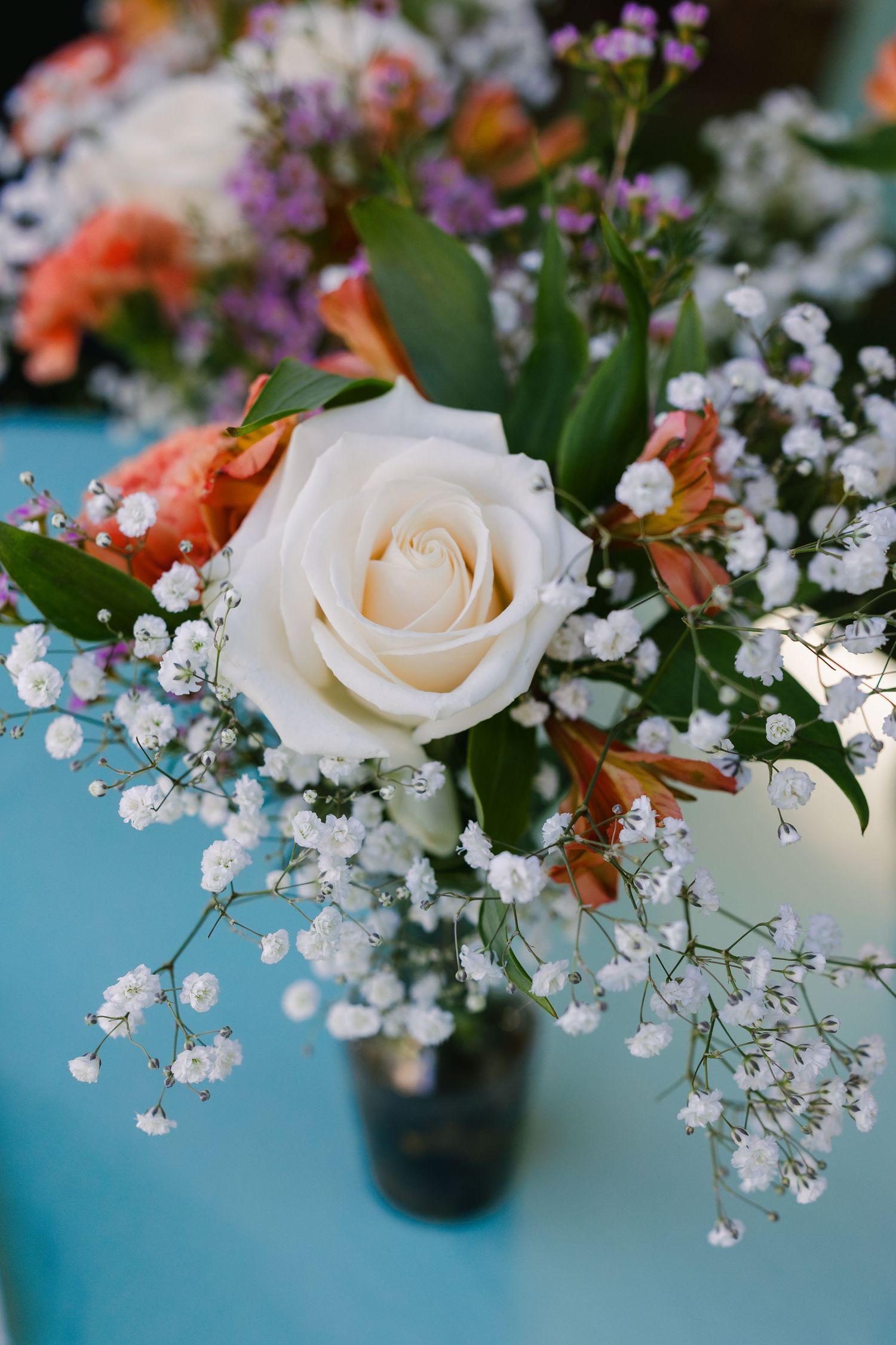 Elegant floral arrangement featuring white roses, baby's breath, and coral blooms against blue background.