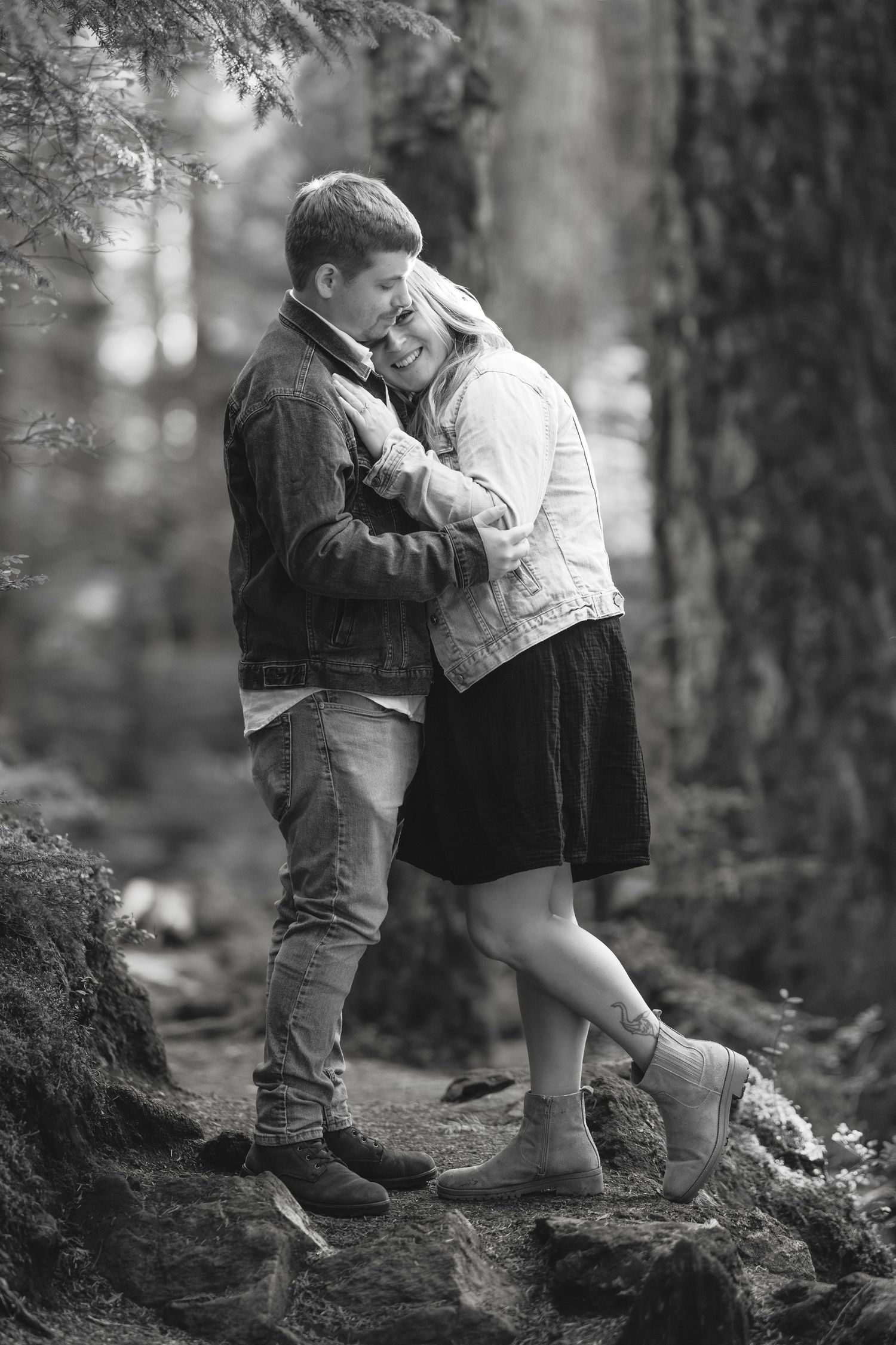 A romantic couple sharing intimate moments on a forest trail in black and white photography.