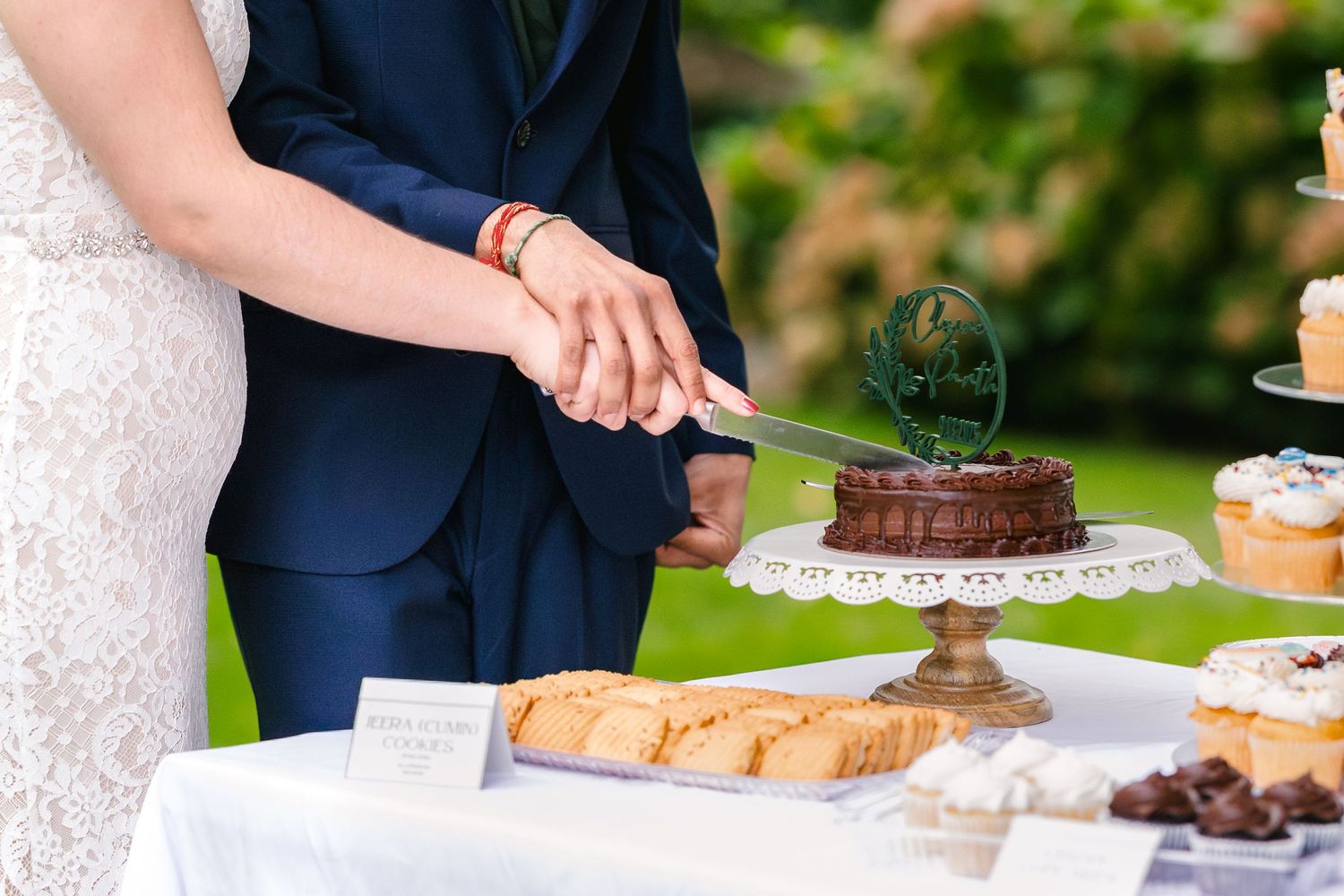 Wedding reception dessert table with guests serving themselves cake and treats in an outdoor garden setting.