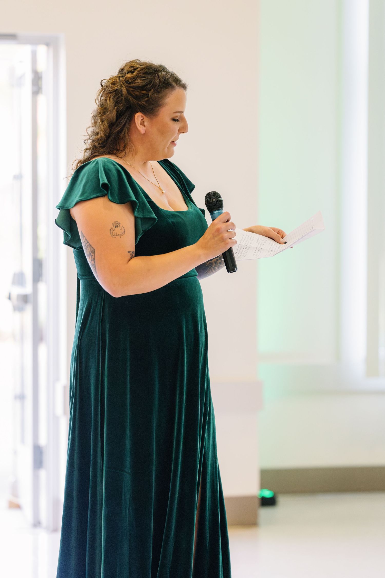 Someone in an elegant emerald green dress delivers a speech with a microphone during a formal event.