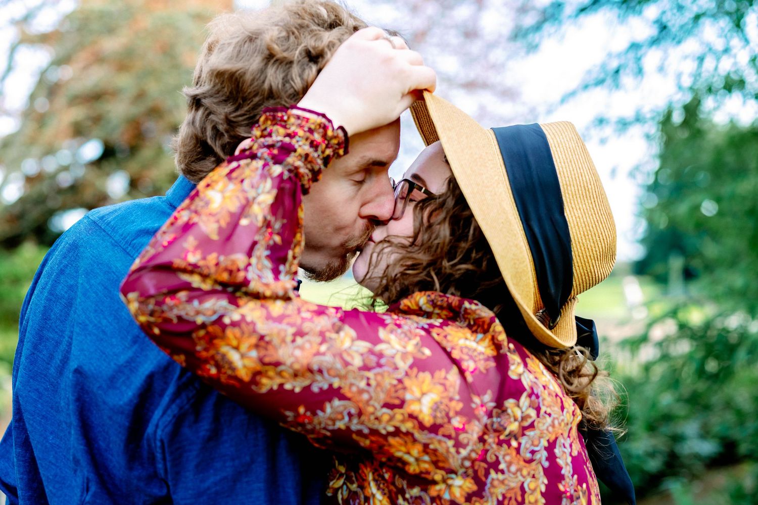 A romantic couple embraces outdoors in a garden setting, with one wearing a floral dress and the other in blue.