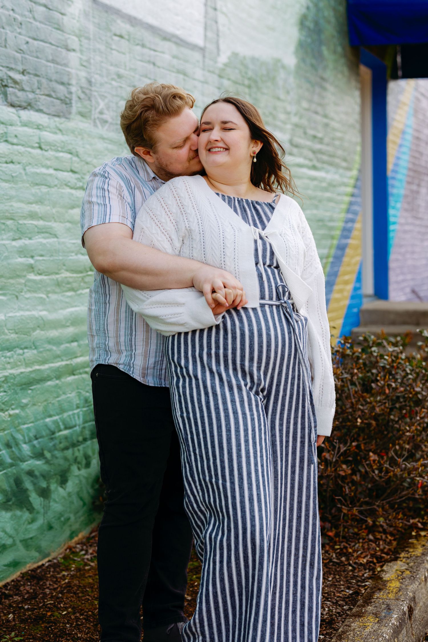 A couple shares an intimate embrace against a mint green brick wall in a series of candid romantic moments.