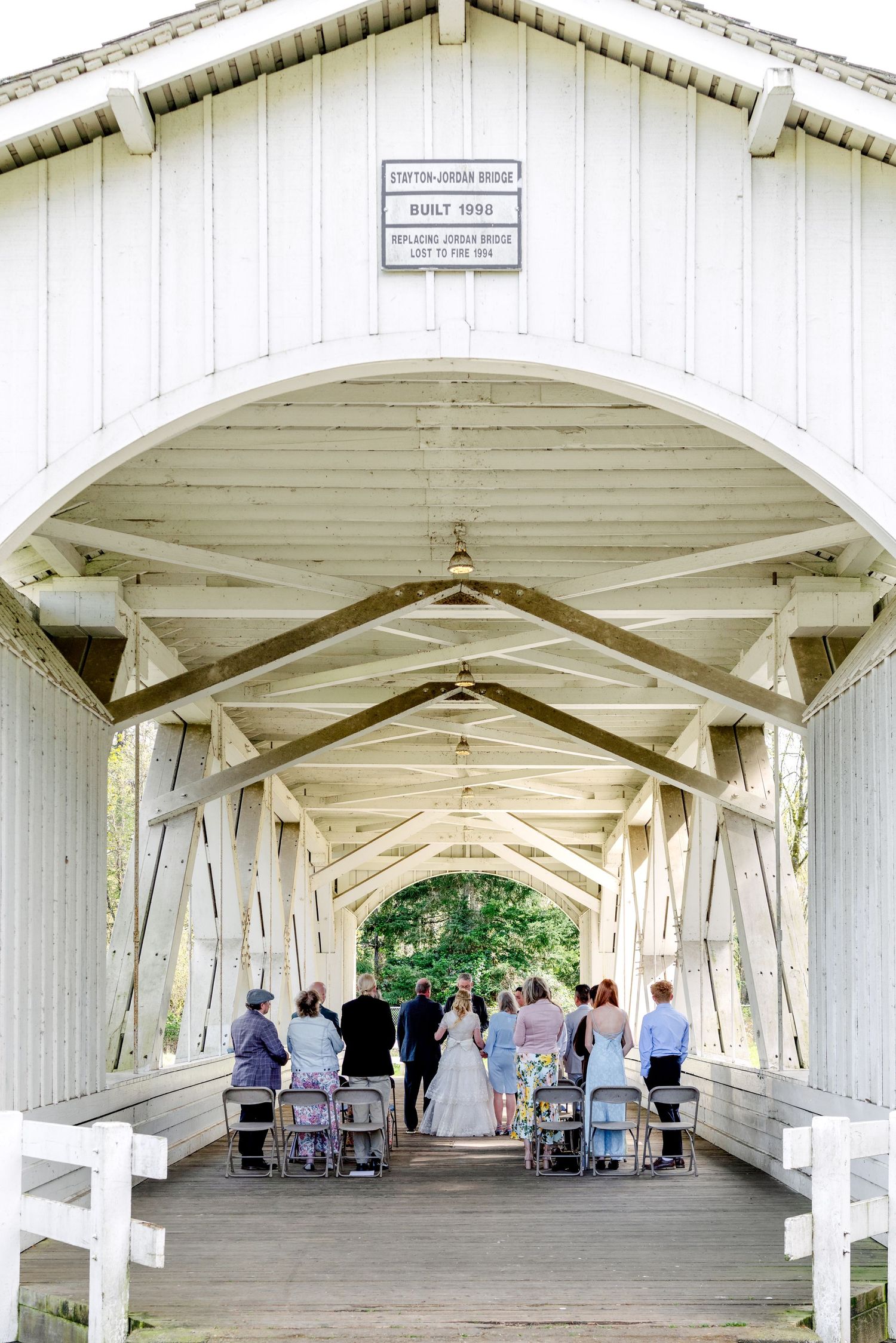 Wedding ceremony inside a white covered bridge with guests seated along the sides.