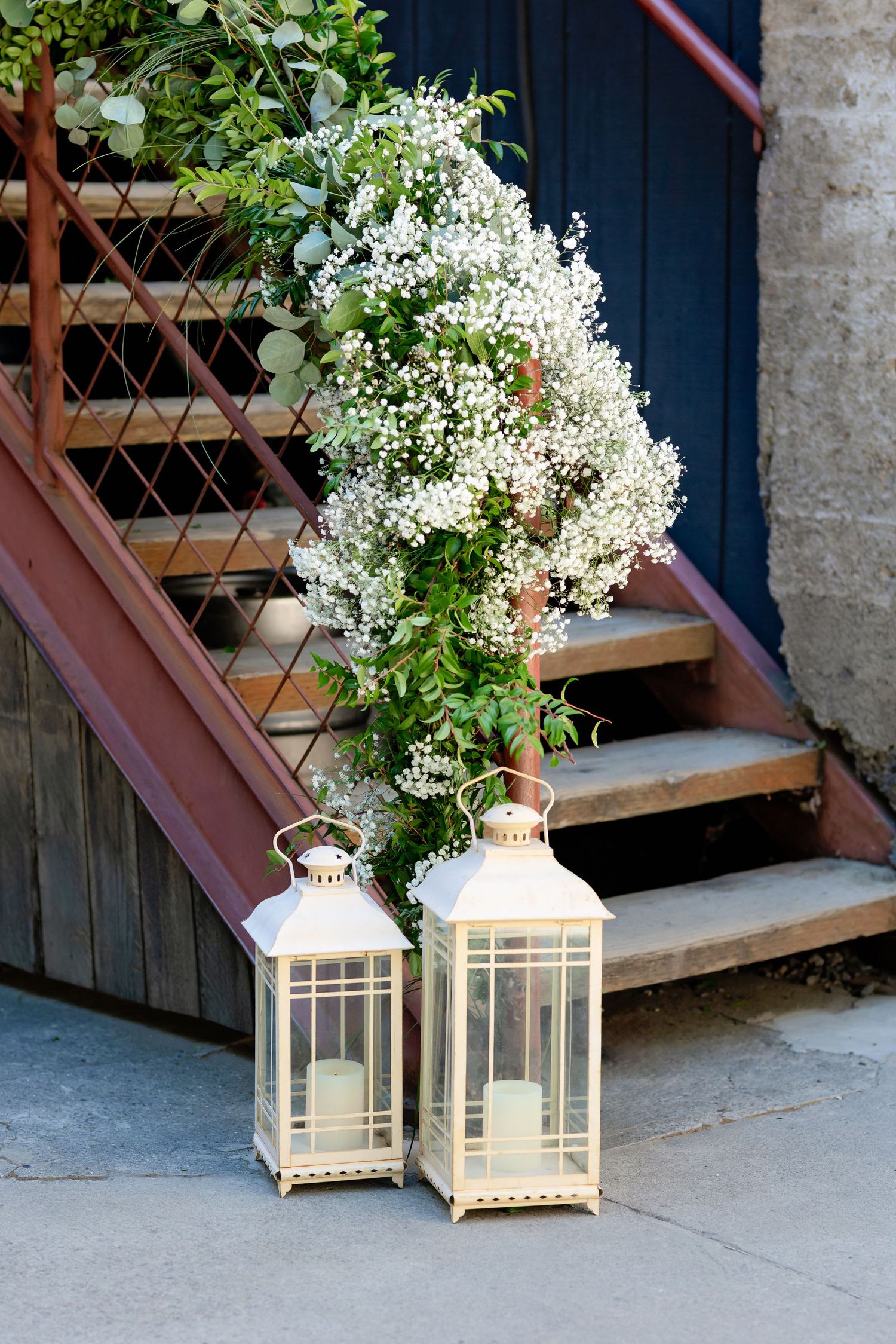 Two white lanterns with candles beside floral arrangement on stone steps.