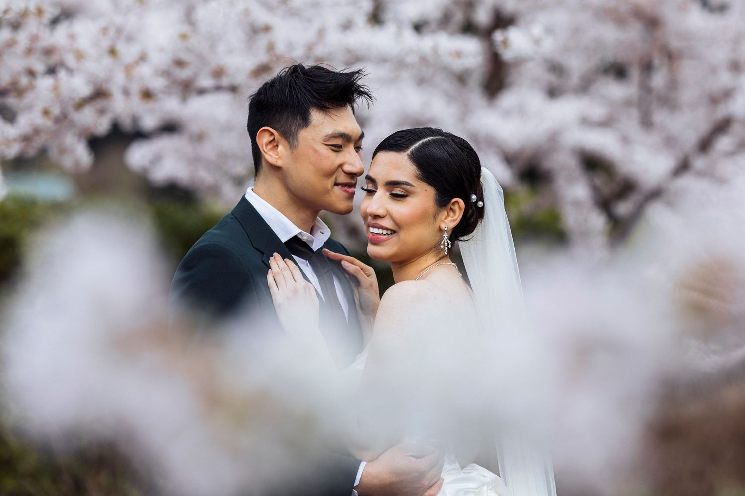 A romantic wedding couple embraces among blooming cherry blossoms in a dreamy spring garden setting.