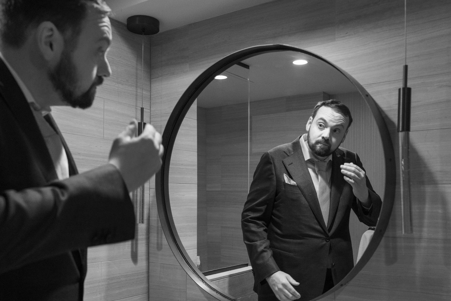 Black and white sequence showing a man adjusting his tie and suit in multiple mirror reflections.