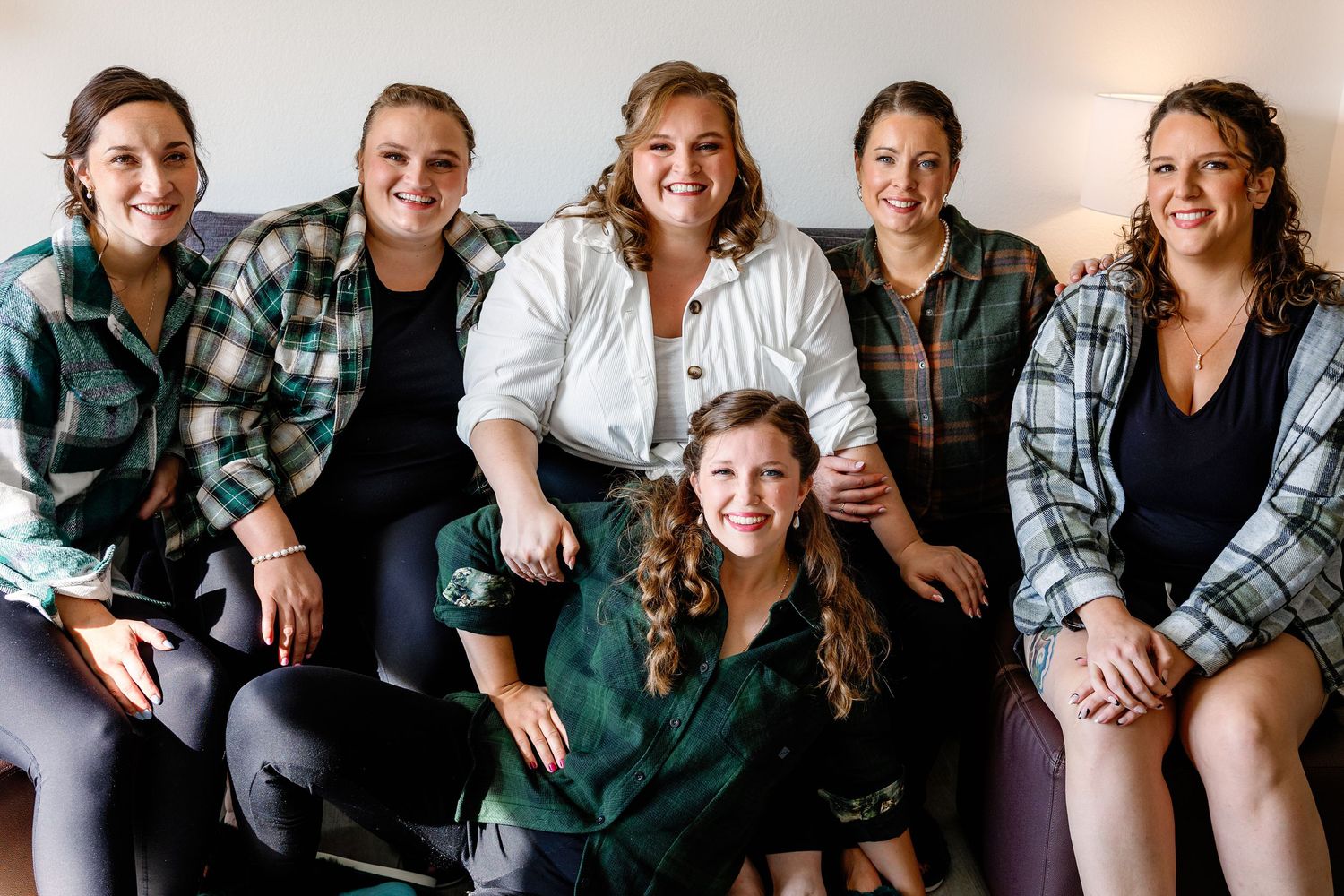 A group of six people sitting together on a couch wearing casual plaid shirts and smiling at the camera.