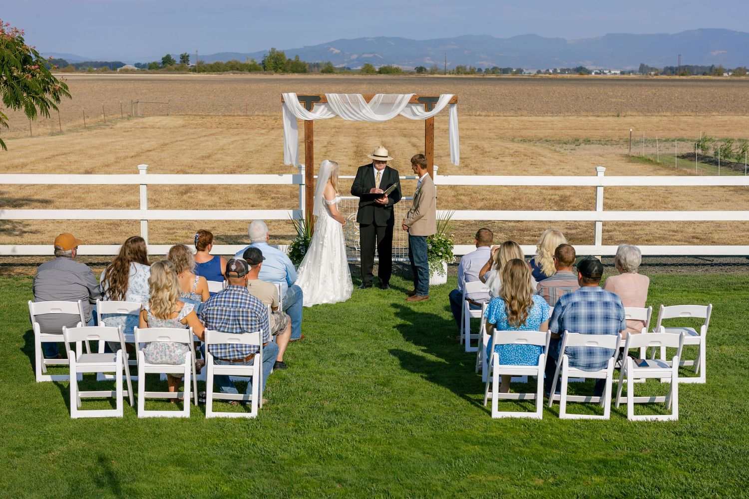 White folding chairs arranged in rows on a green lawn for an outdoor wedding ceremony with distant mountain views.