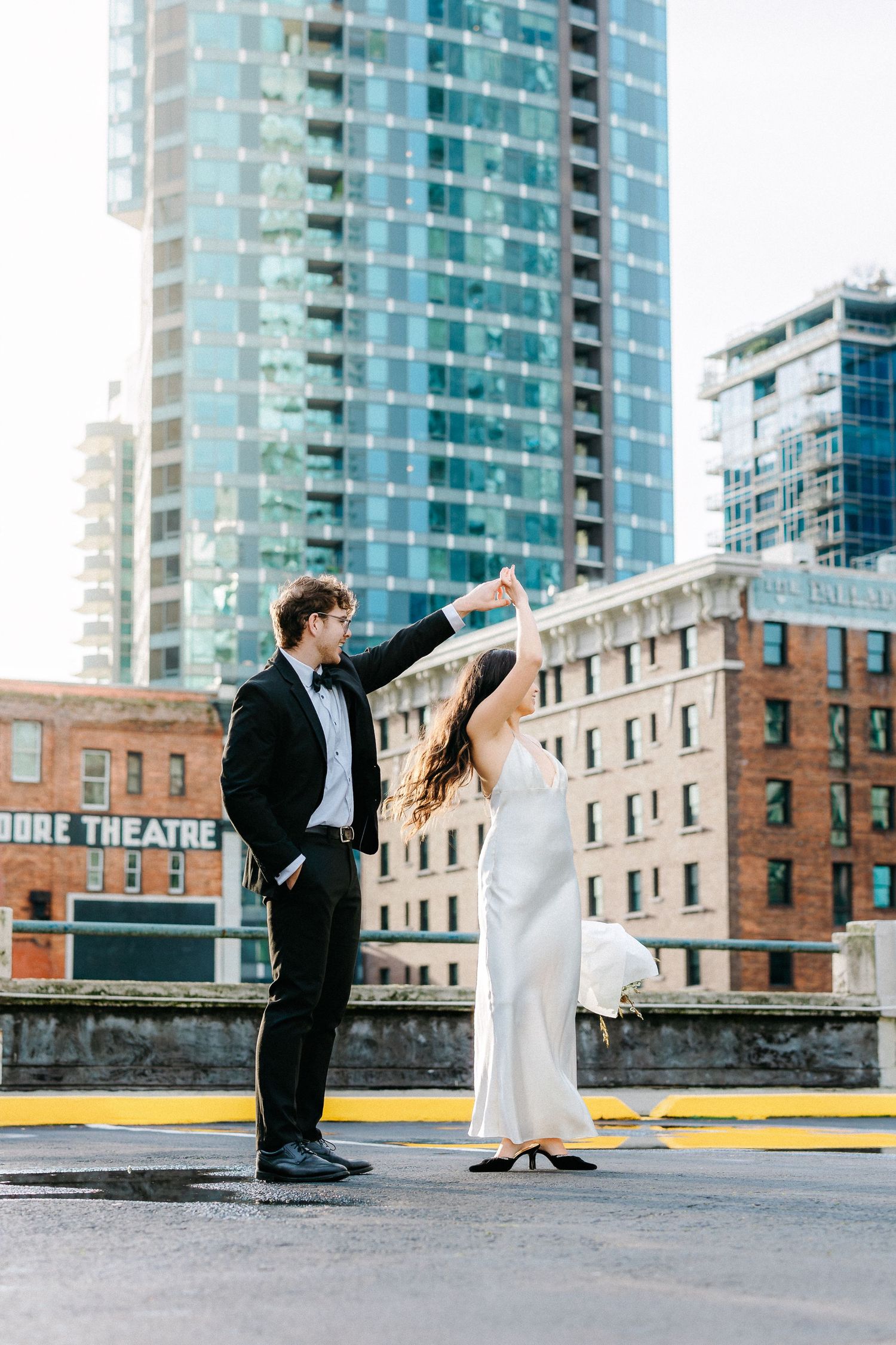 Couple dancing on urban rooftop with high-rise buildings in background.