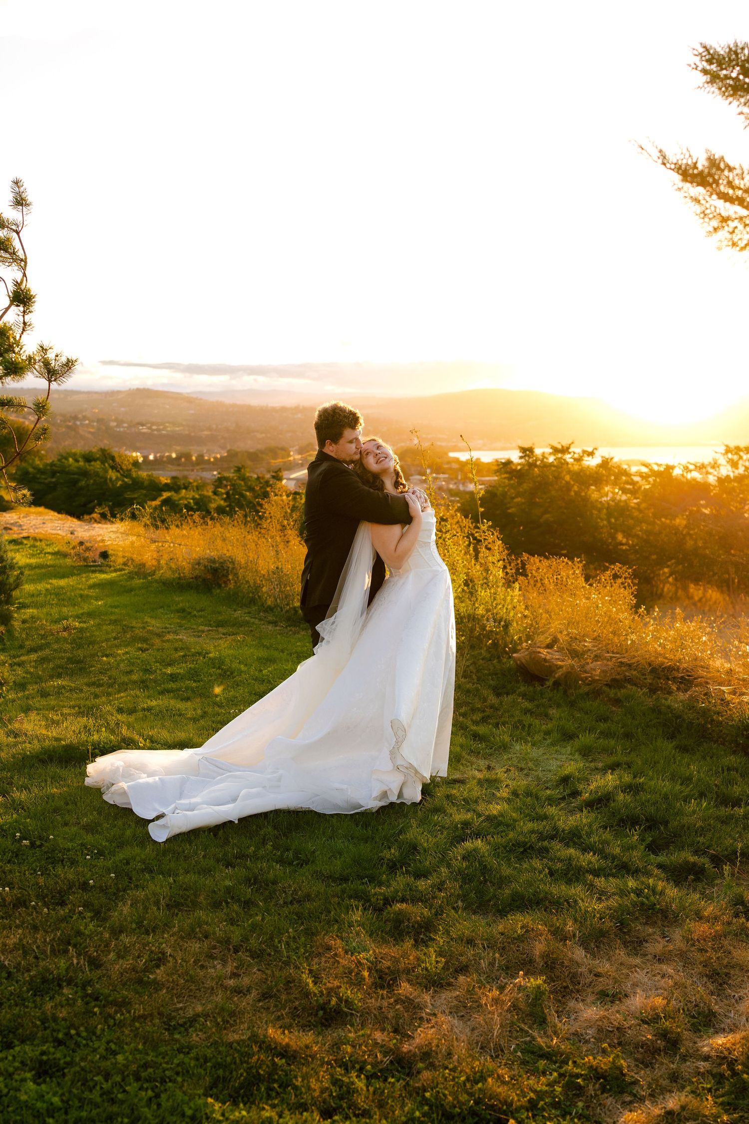 Wedding couple embracing on a hilltop during golden hour with flowing white dress and scenic backdrop.