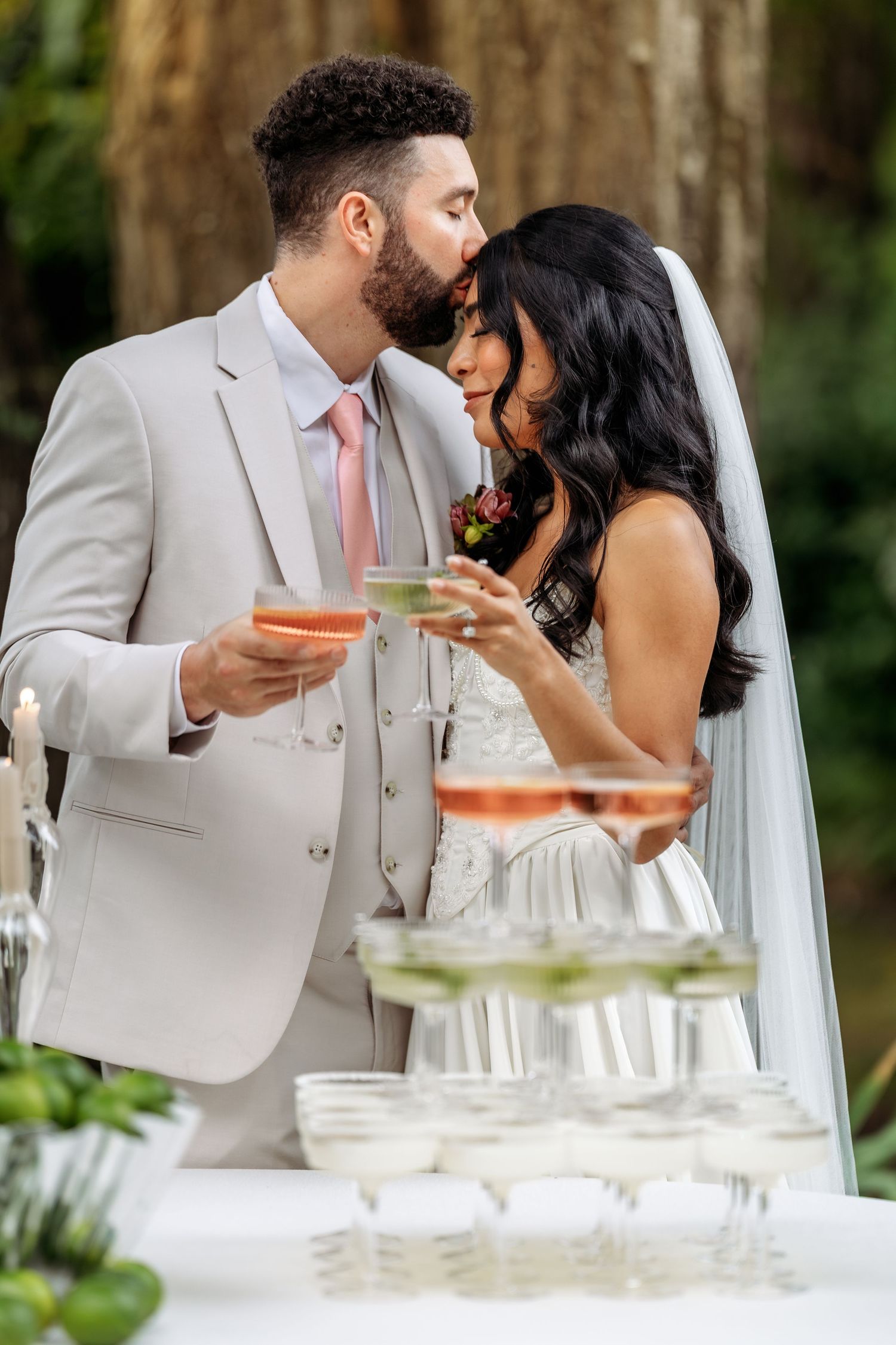 Couple shares intimate moment at elegant outdoor wedding reception with drinks and table settings.