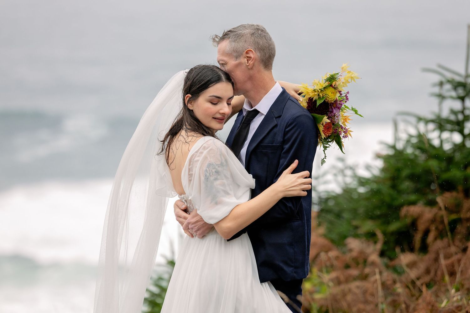 A couple shares an intimate moment during their wedding on a cloudy day in a scenic outdoor setting.