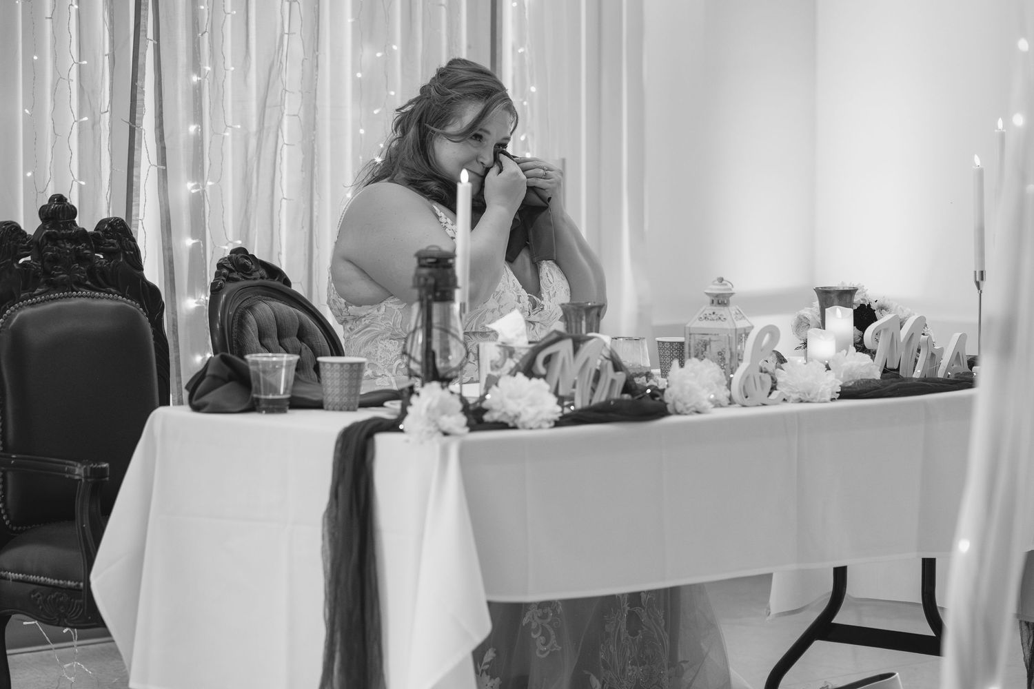 Black and white photo of someone seated at decorated wedding reception table.