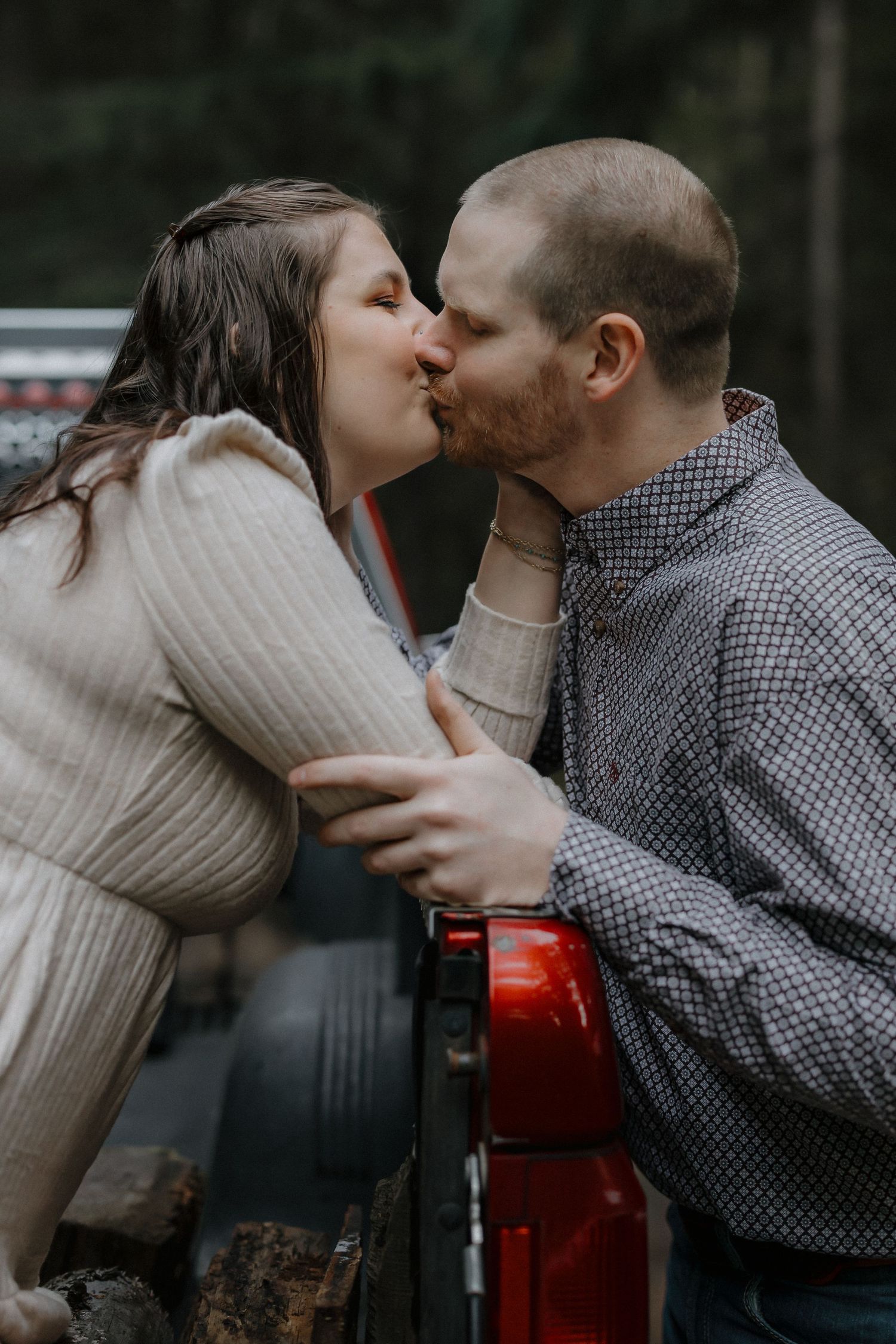 A tender moment shared between a couple in warm sweaters against a red truck bed.