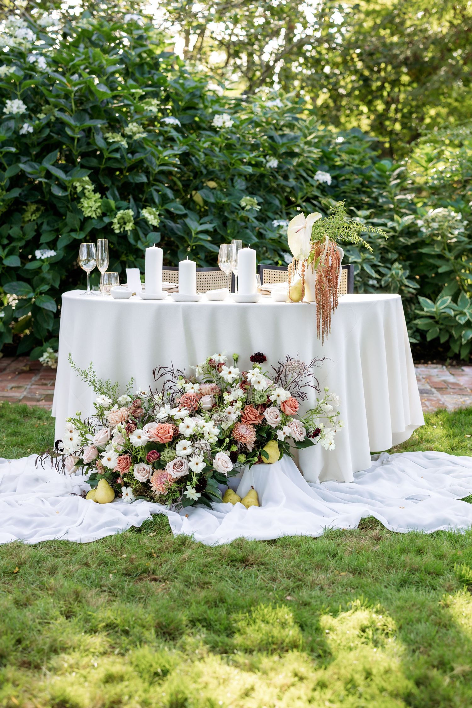 Elegant outdoor wedding reception tables with white linens and floral arrangements in a garden setting.