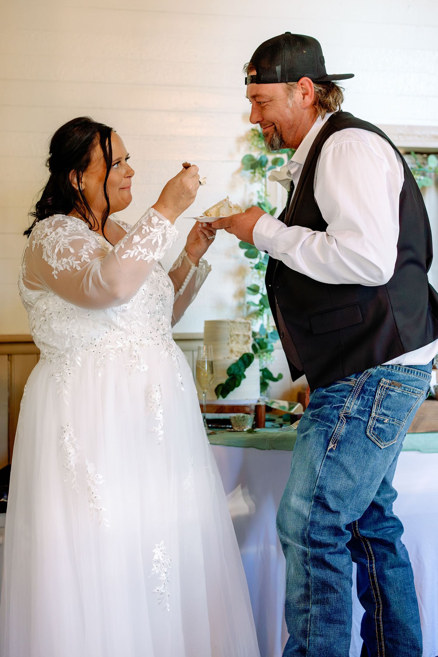 A playful wedding cake-feeding moment between a couple in casual western attire.