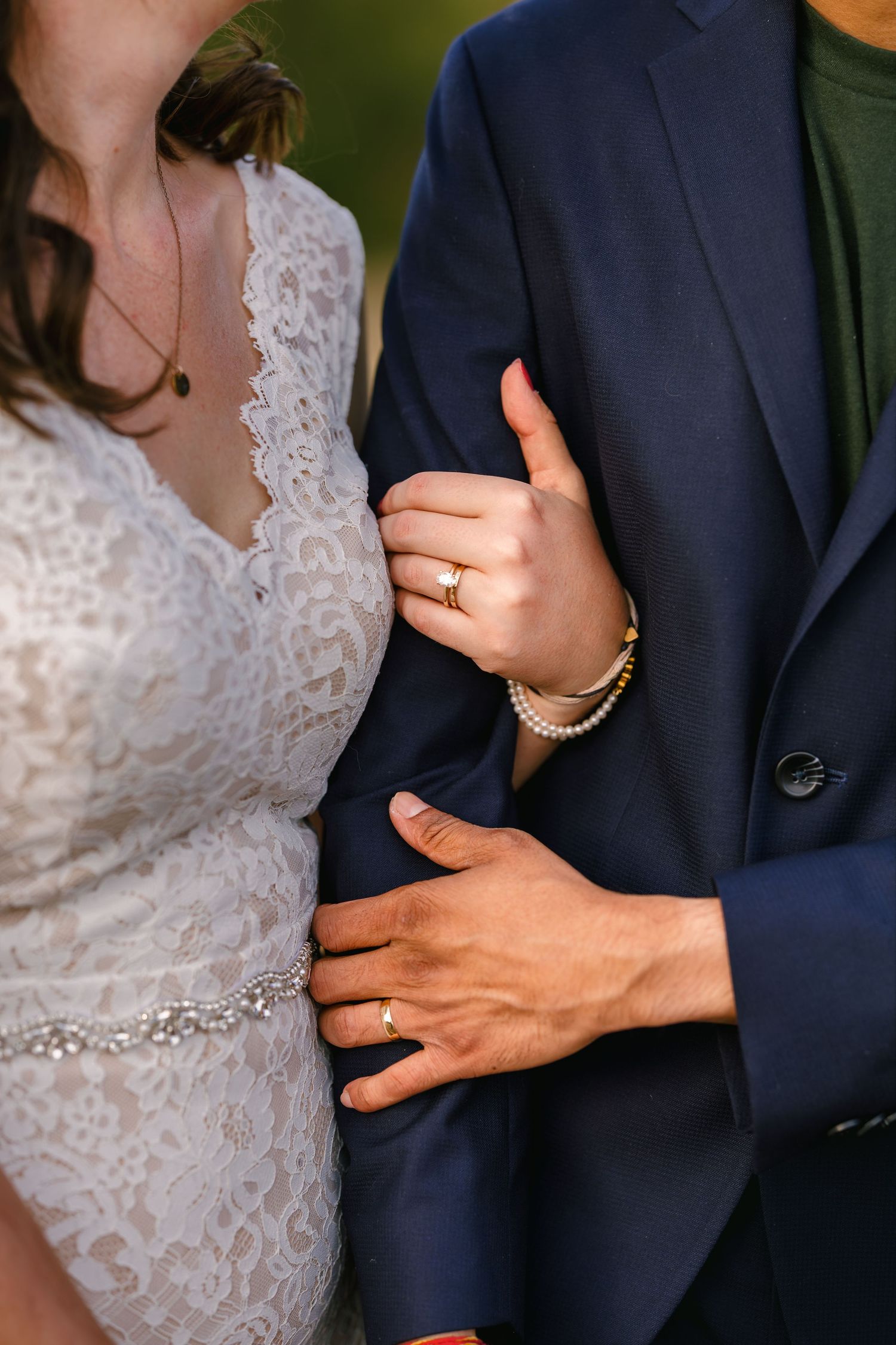 Close-up details of wedding attire showing lace dress and navy suit with hands embracing.