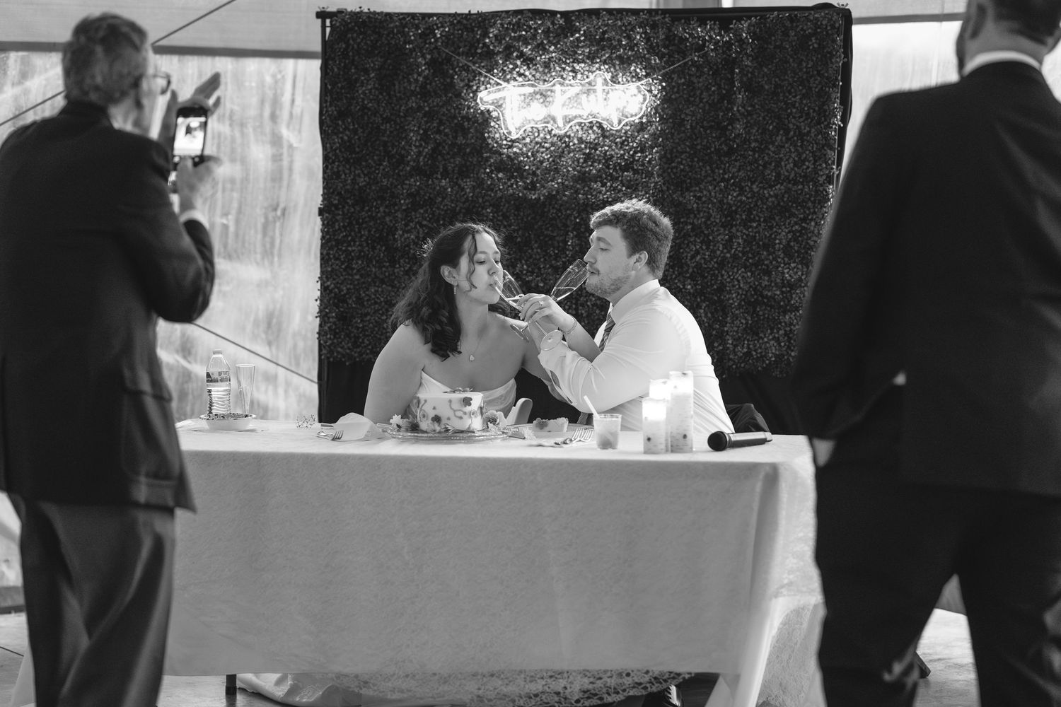 Black and white reception photo showing tables with white linens and formal place settings.