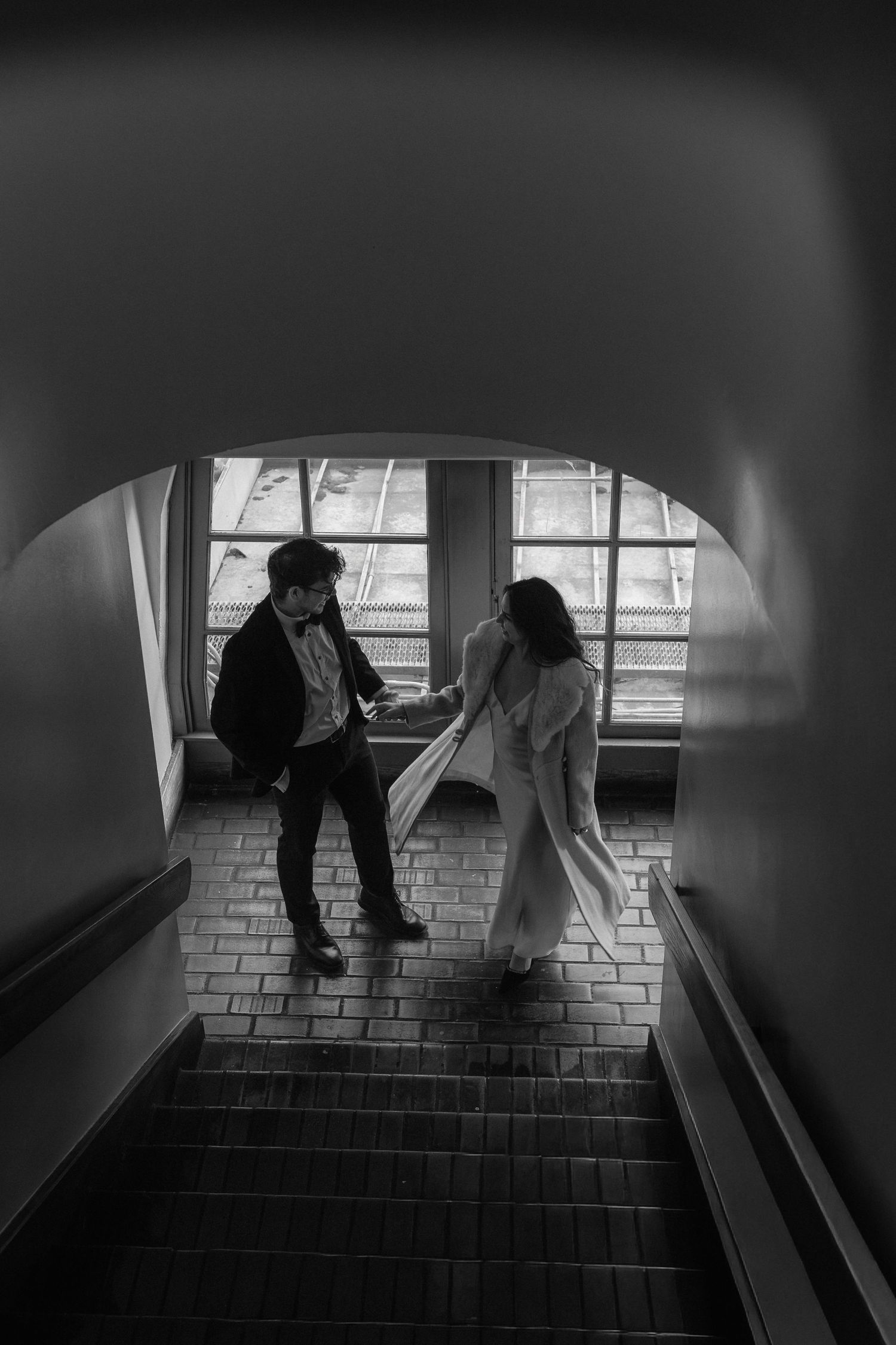 Black and white sequence of figures descending stairs in a dimly lit interior space.