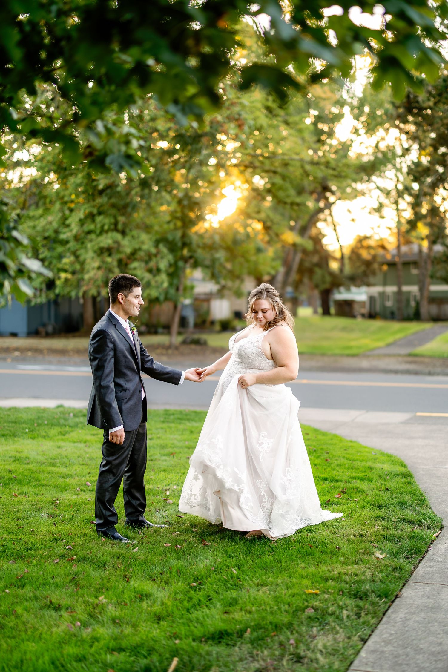Newlywed couple poses playfully on grass during golden hour wedding photoshoot.