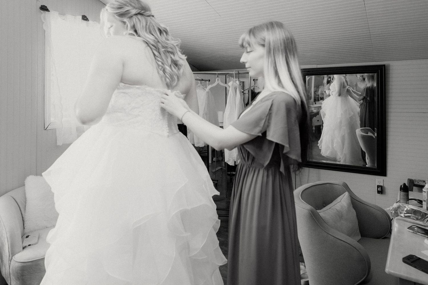 Bridesmaid helping bride with wedding dress in a bridal suite, captured in elegant black and white photography.
