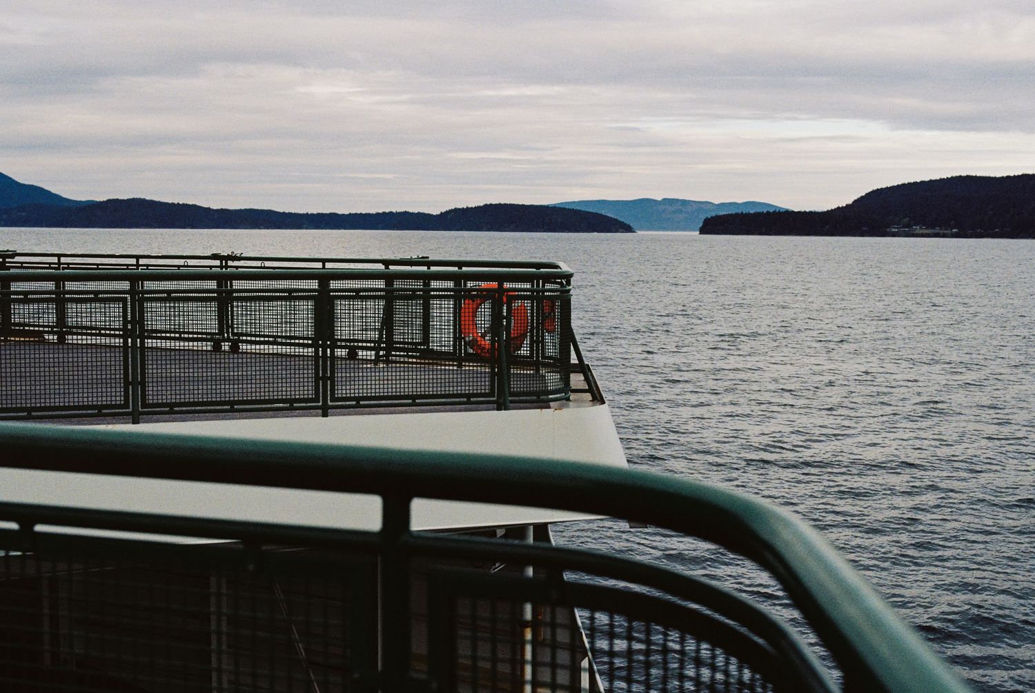 View from a ferry deck overlooking calm fjord waters with mountains and islands in the distance.