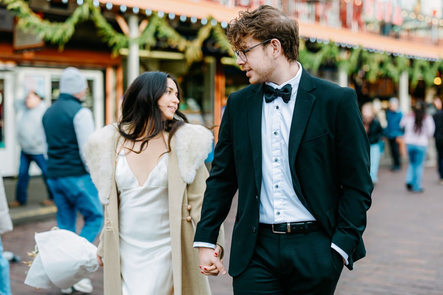 A stylish couple in formal wear strolling through a festive marketplace.