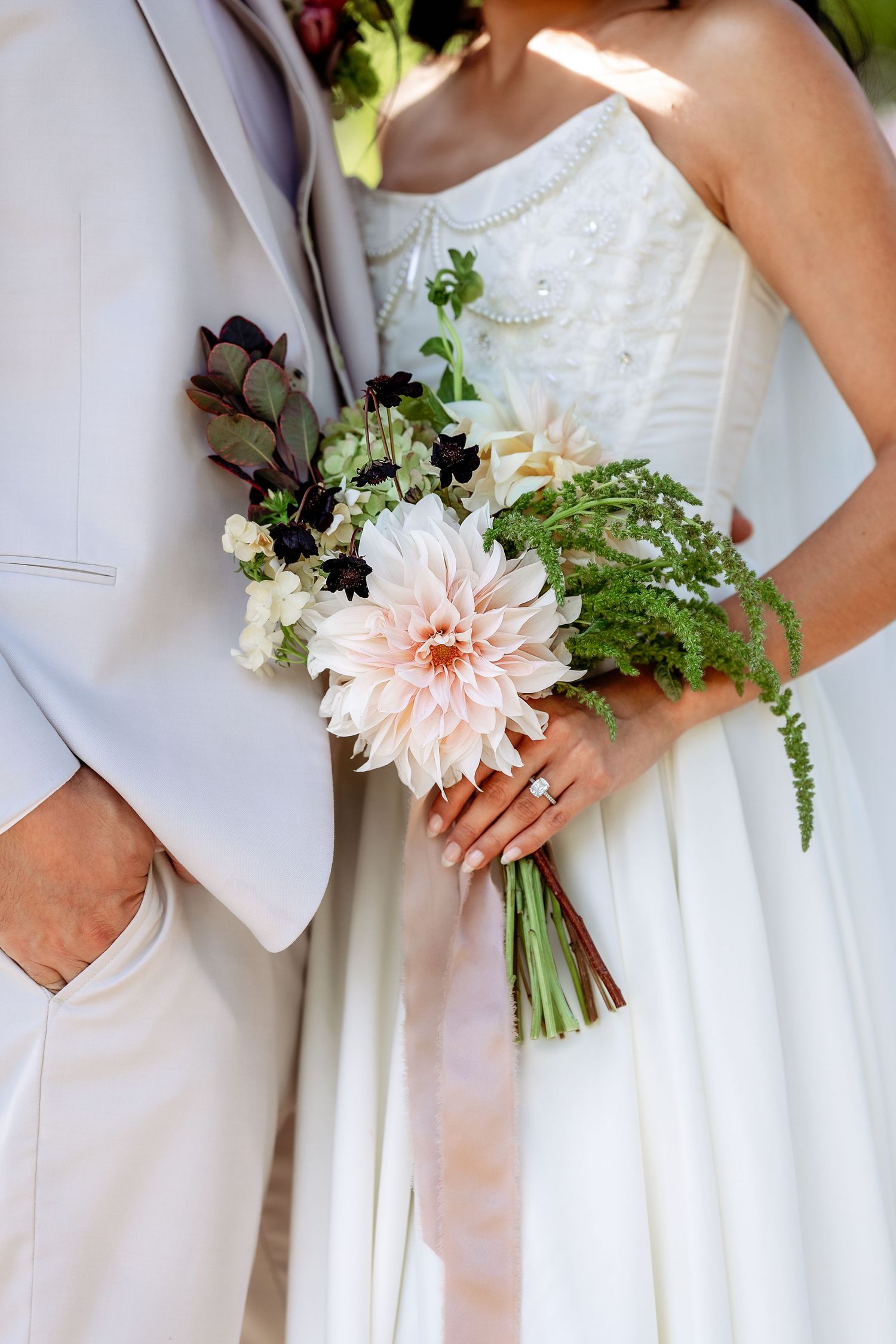 Close-up details of white wedding attire and delicate pink floral bouquet with greenery.