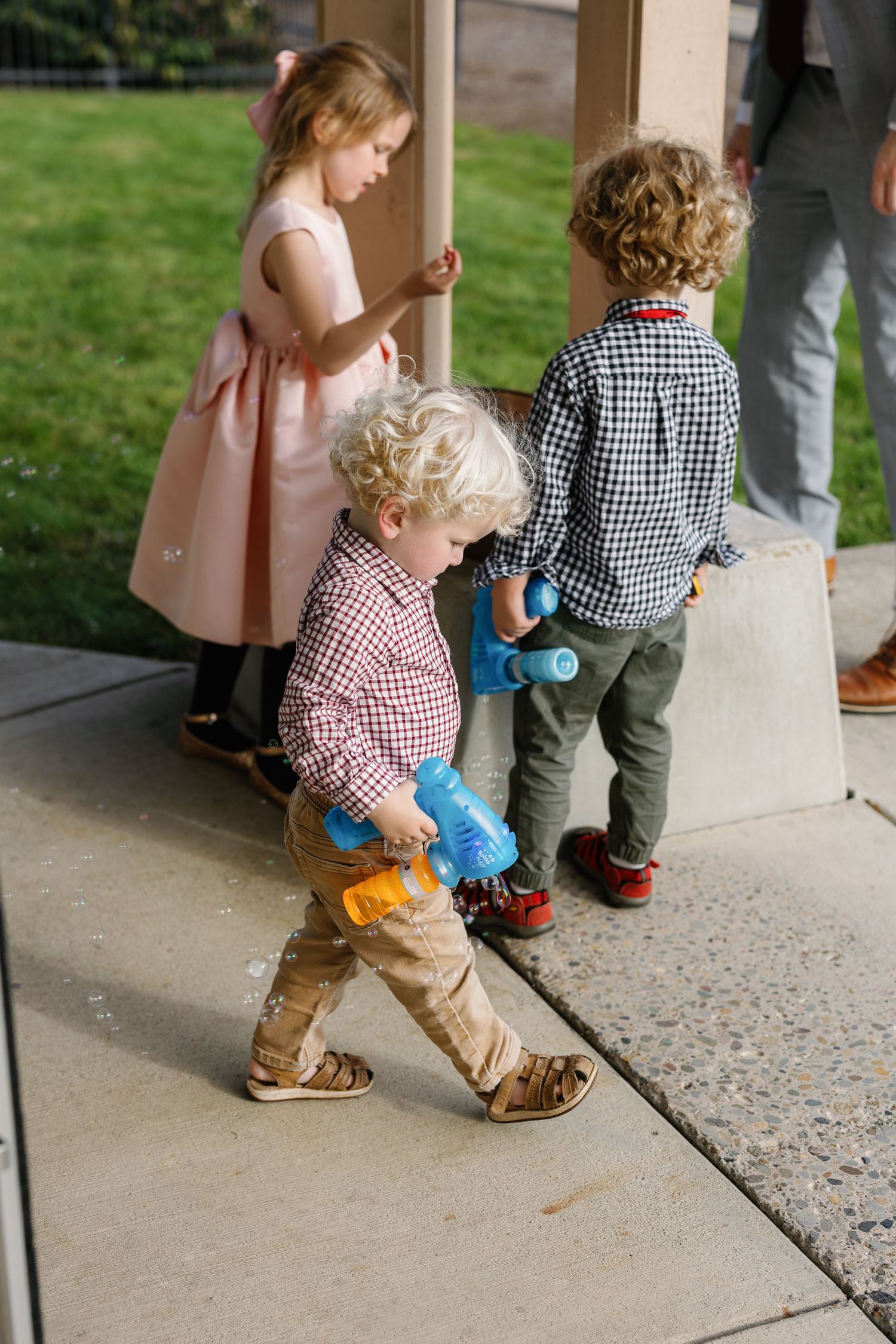 Young children in casual clothing standing on a concrete porch near a grassy lawn.