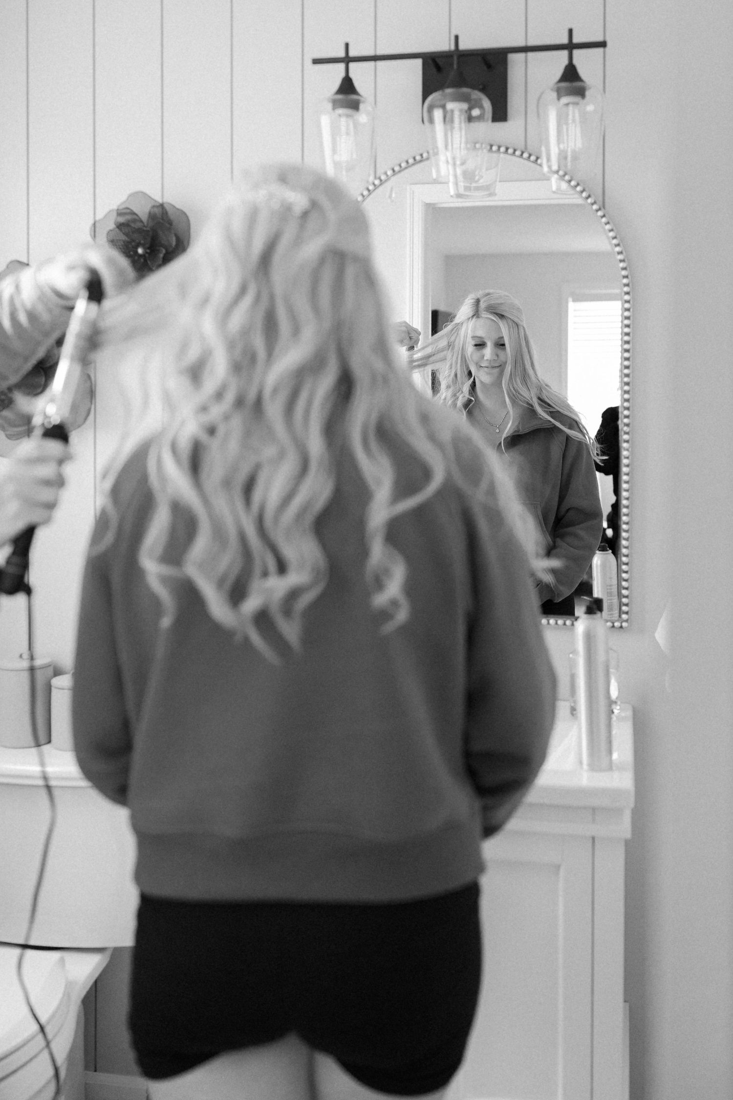 Black and white photo of someone getting ready at a vanity with mirrors and lights.