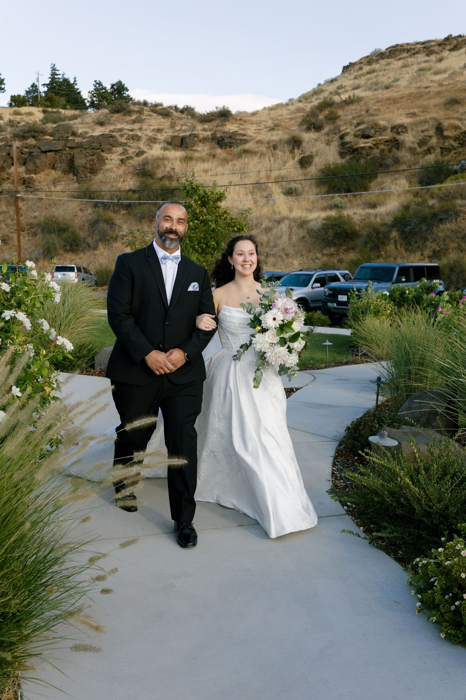 Wedding couple sits on concrete steps with desert hills in background during outdoor photoshoot.