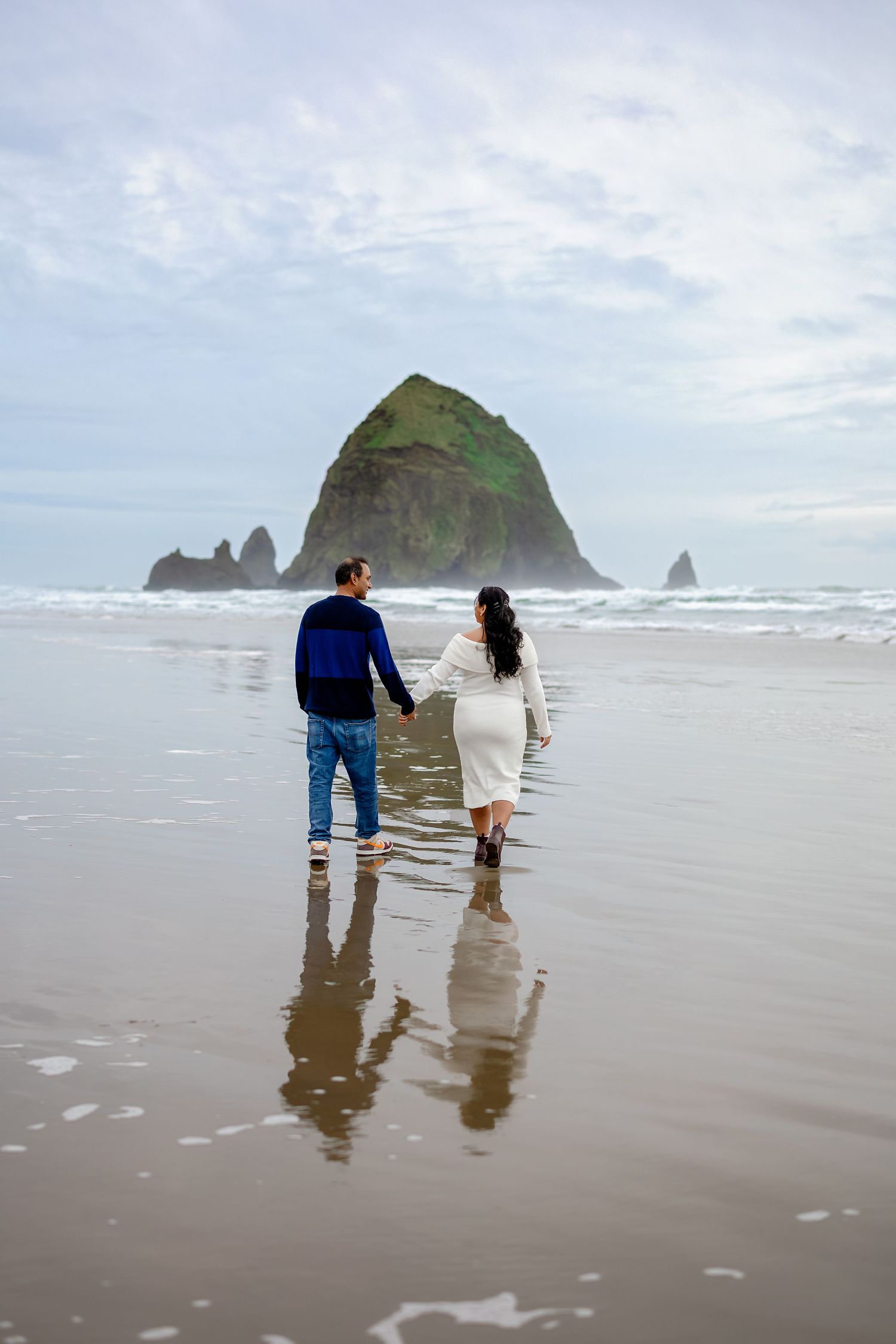 A couple walks together on a misty beach with Haystack Rock visible in the background at Cannon Beach.