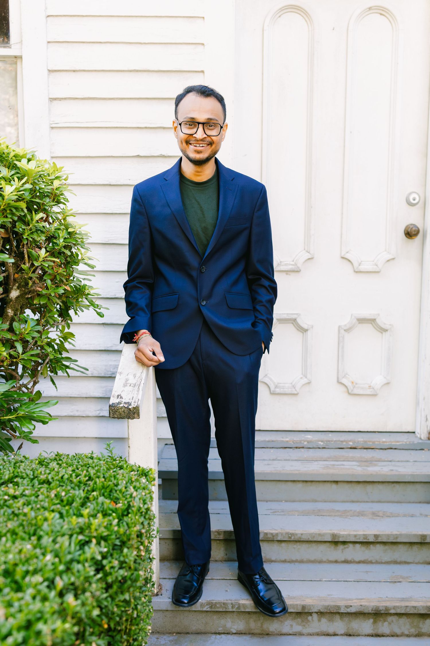 Person in a navy blue suit standing on white porch steps.
