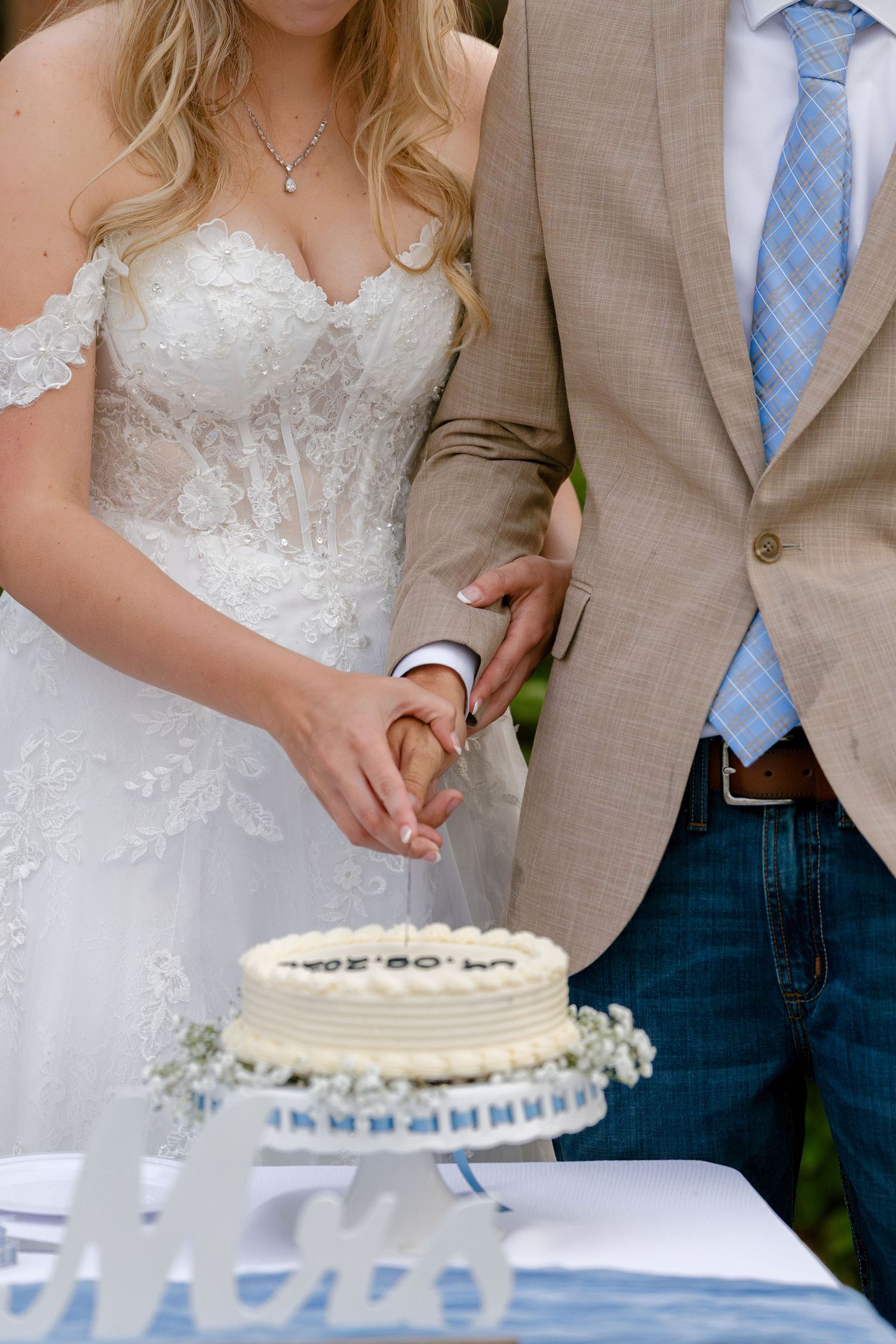 A couple in wedding attire cutting their white wedding cake together.