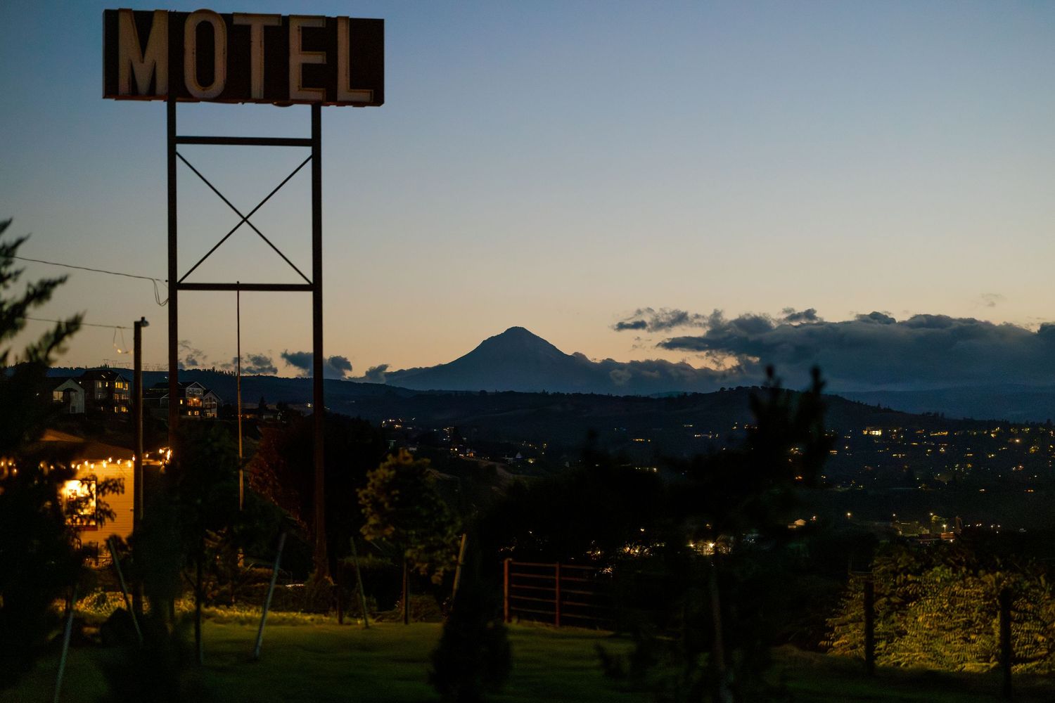 Vintage motel sign silhouetted against a mountain landscape at dusk.
