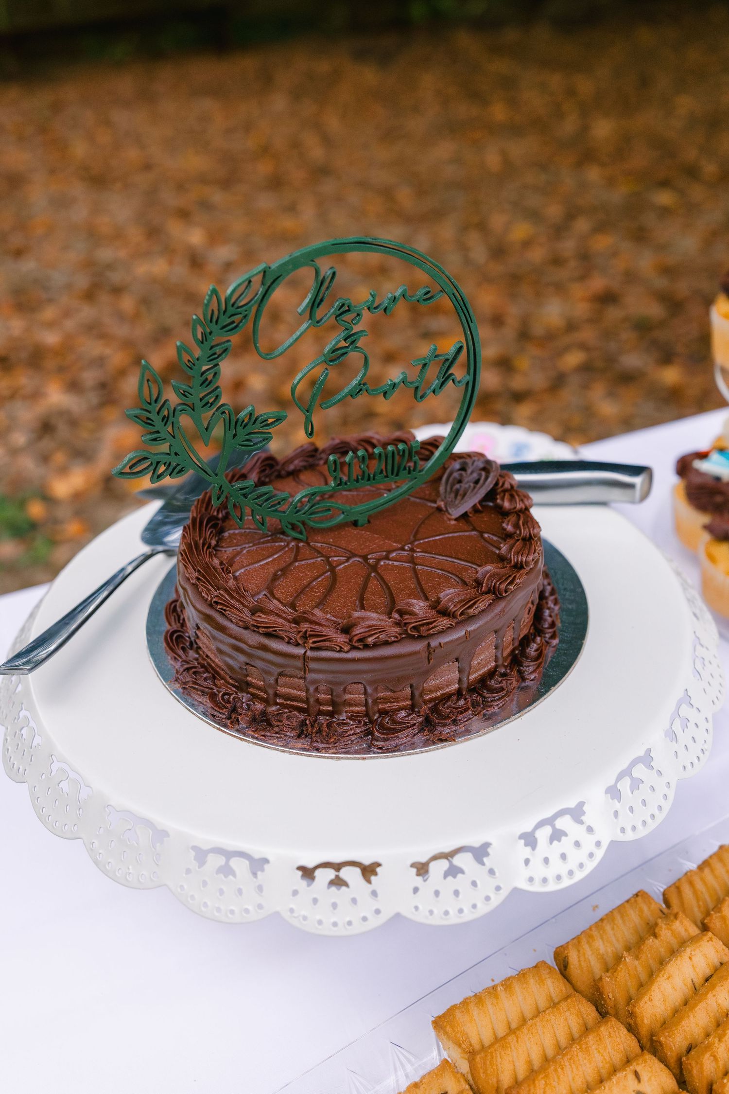 Chocolate cake with decorative green topper sits on white doily against brown autumn leaves background.
