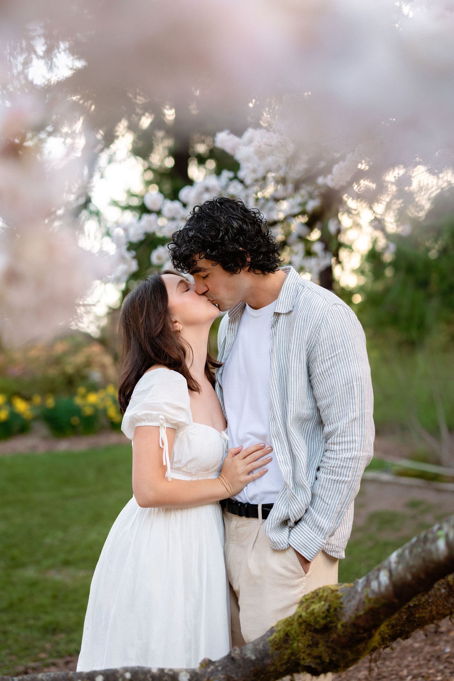 A romantic couple embraces in a dreamy outdoor setting with soft lighting and cherry blossoms in the background.