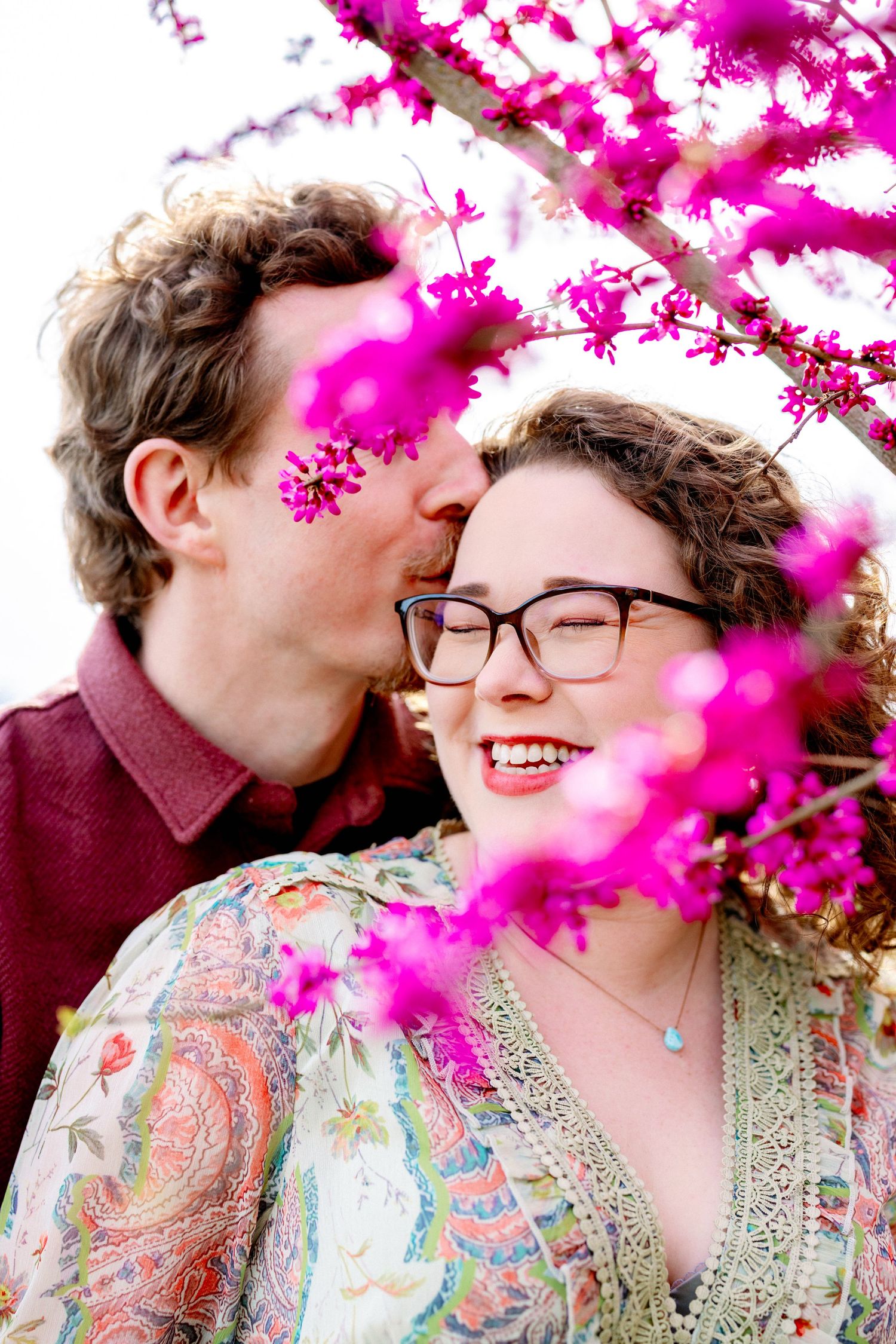 Intimate couple portraits framed by vibrant pink cherry blossoms in spring.