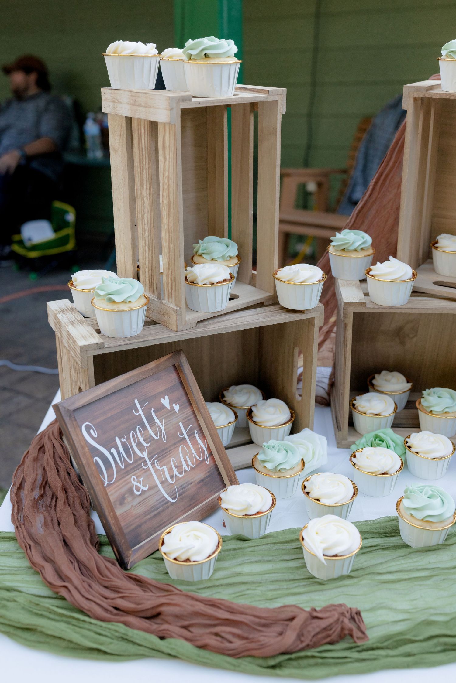 Tiered wooden crate display of white and mint frosted cupcakes with Sweets & Treats sign.