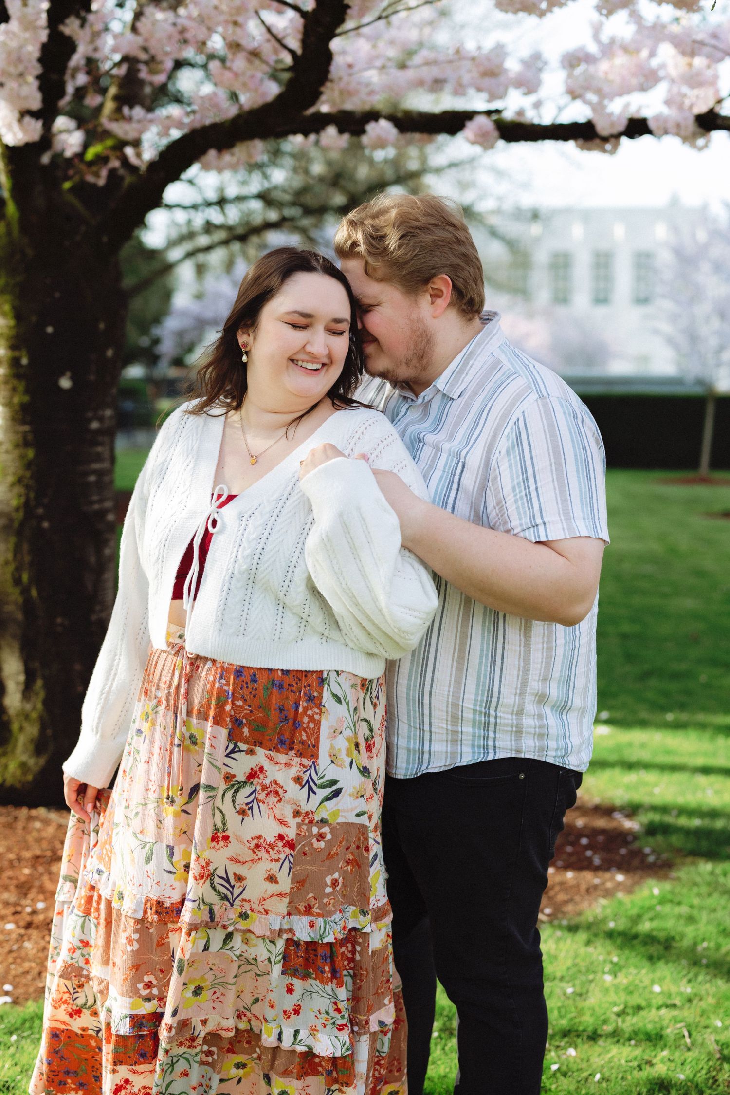A couple shares romantic moments under blooming cherry blossom trees in a spring garden setting.