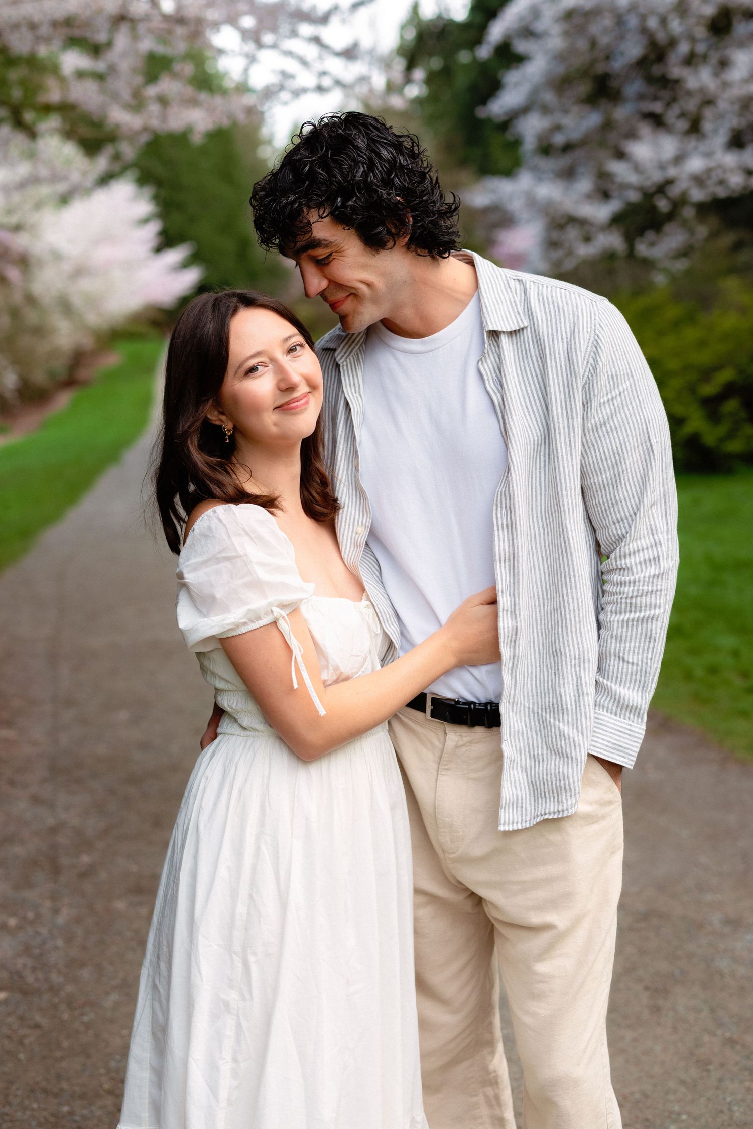 A romantic moment shared between a couple under flowering cherry blossoms on a garden path.