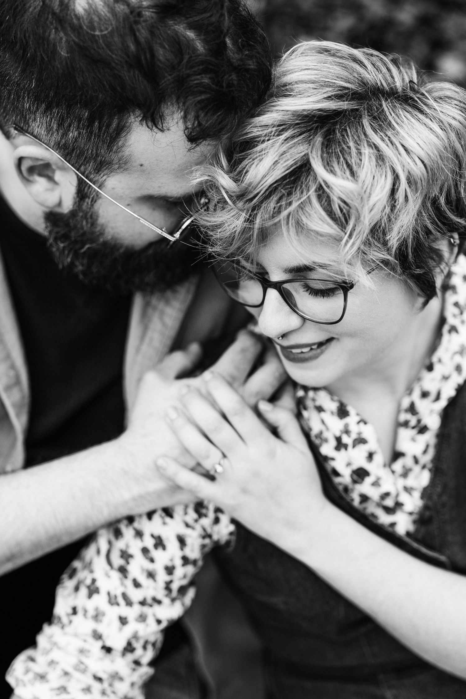 Black and white intimate portrait of couple sharing tender moment, with glasses and floral dress details.