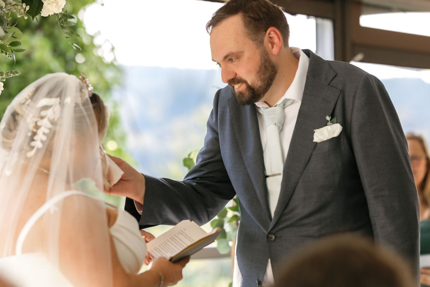 Outdoor wedding ceremony under a covered pavilion with natural greenery in background.