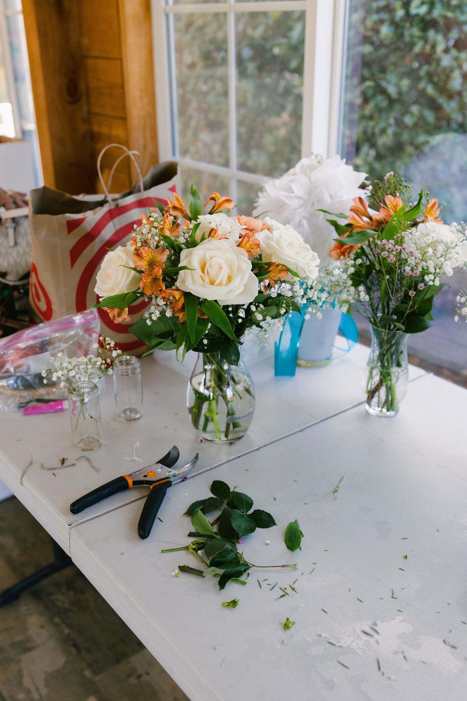 Fresh floral centerpieces in glass vases line white table at wedding reception.